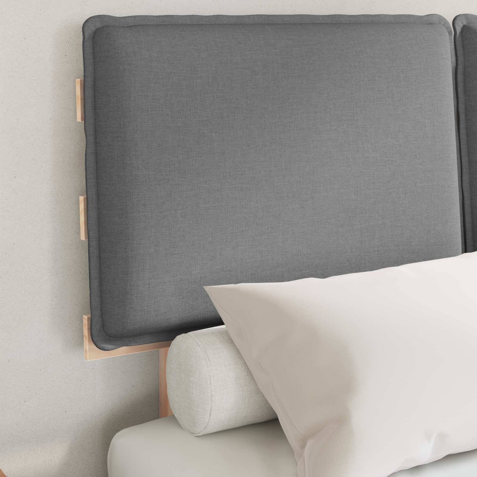 Graue gepolsterte Kopfteile mit einem weißen Kissen und einem Nackenrolle auf einem Bett vor einer hellen Wand.