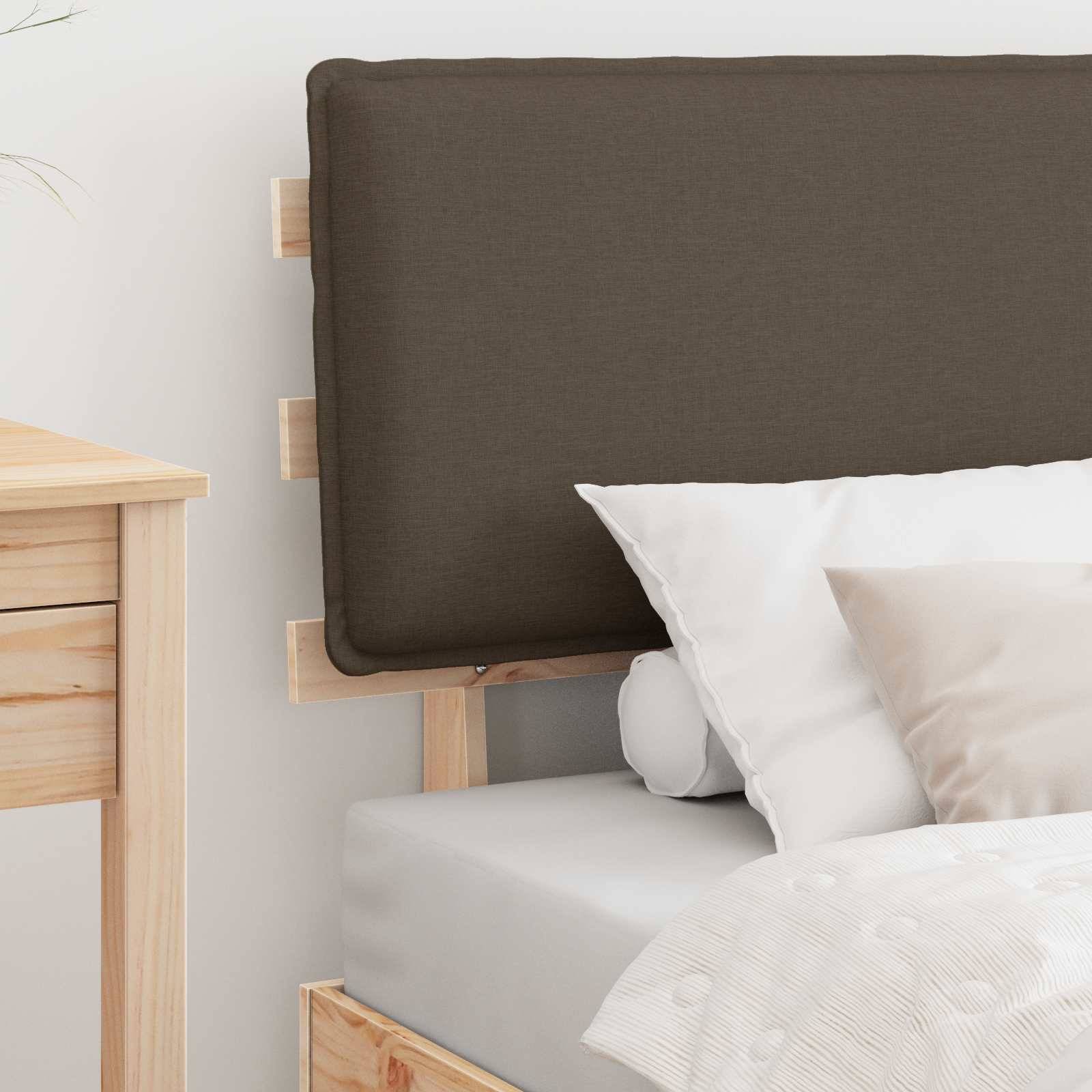 Ein ordentlich gemachtes Bett mit einem beigen Kopfteil, zwei weißen Kissen und einem beigen Kissen. Auf der linken Seite ist ein kleiner Holz-Nachttisch teilweise zu sehen.