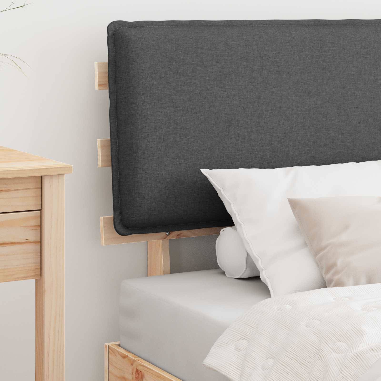 Ein ordentlich gemachtes Bett mit einem grauen Kopfteil und weißen Kissen, das sich in einem hellen Raum mit einem hellholzigen Nachttisch befindet.