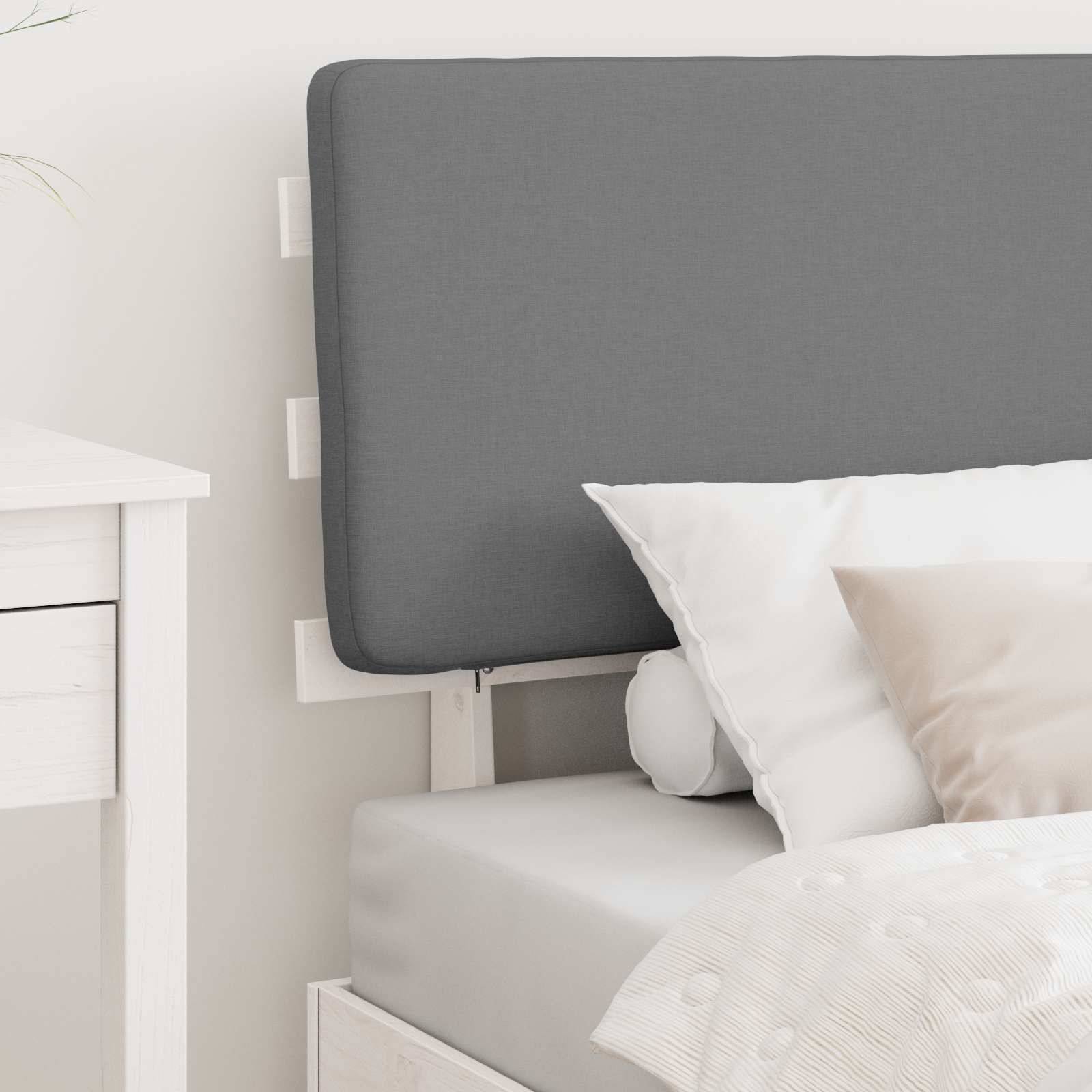 Ein ordentlich gemachtes Bett mit einem hellgrauen Kopfteil, weißen Kissen und einer weißen Steppdecke. Ein kleiner weißer Nachttisch ist teilweise zu sehen.
