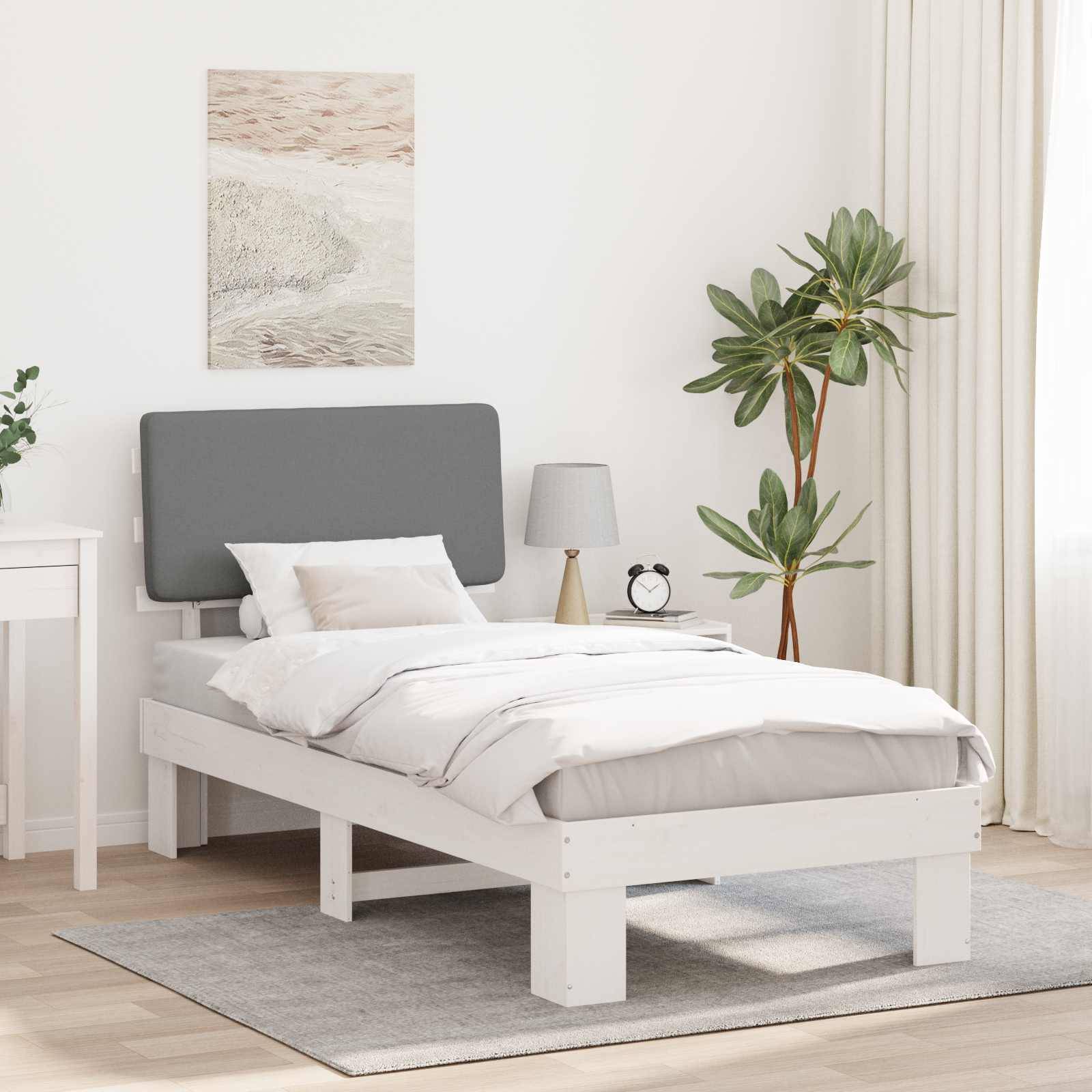 Ein modernes Schlafzimmer mit einem weißen Bett, grauem Kopfteil, kleinem weißem Nachttisch und großer Zimmerpflanze. Licht fällt durch transparente Vorhänge herein.