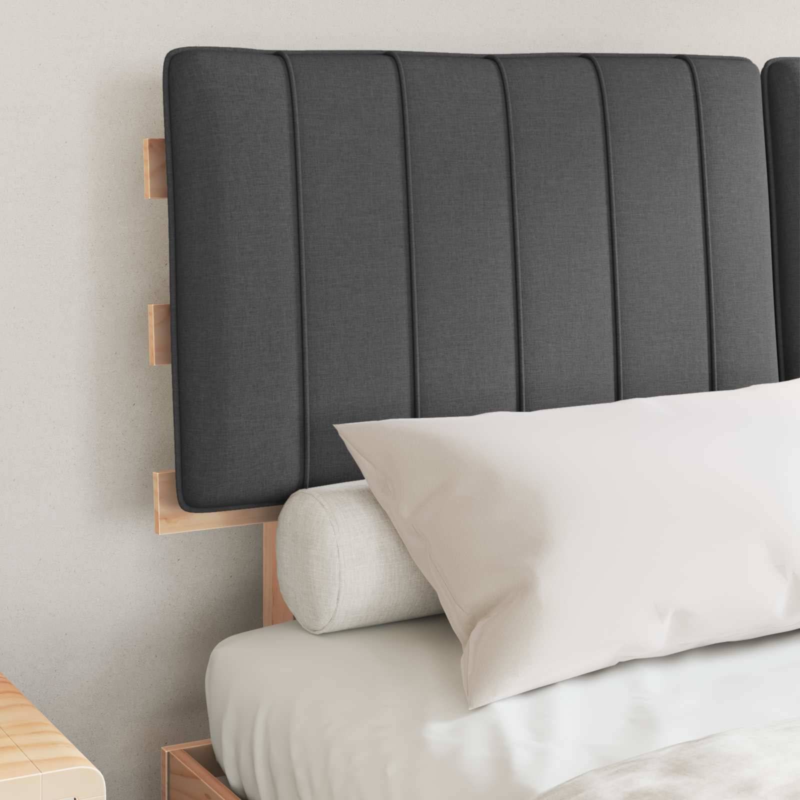 Dunkelgrauer Polsterkopfteil mit vertikalen Nähten, über einem weißen Bett mit passenden Kissen und einem zylindrischen Nackenrolle.