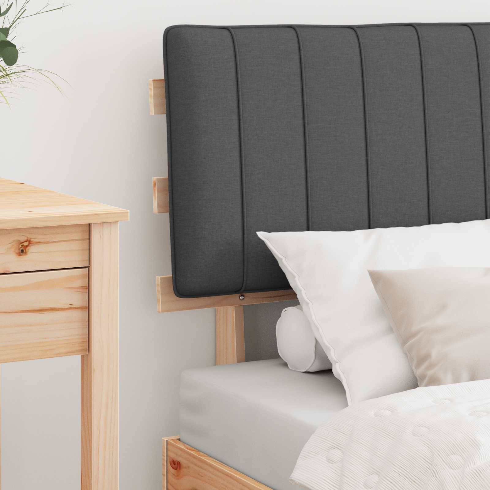 Ein Bett mit einem grau gepolsterten Kopfteil und weißen Kissen steht neben einem hellholzfarbenen Nachttisch mit einer kleinen Schublade.