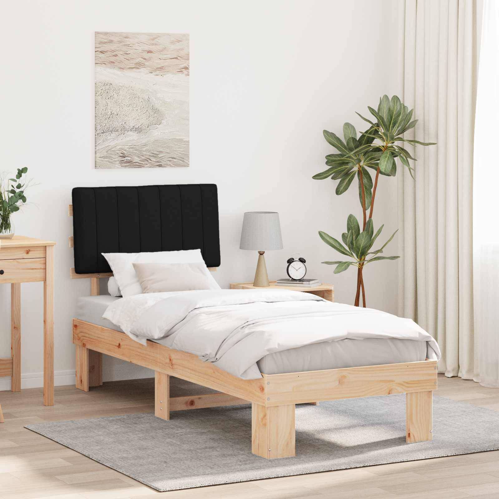 Schlafzimmer mit Holzbettgestell, grauer Bettwäsche, kleinem Nachttisch mit Lampe, grüner Zimmerpflanze, Kunstwerk an der Wand und natürlichem Licht.