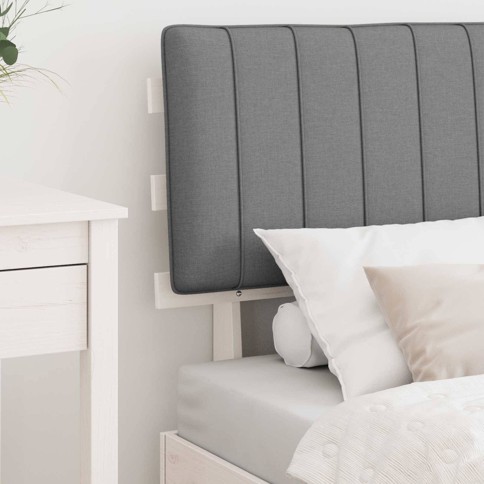 Ein ordentlich gemachtes Bett mit einem hellgrauen gepolsterten Kopfteil, weißen und beigen Kissen und einem weißen Nachttisch in einer minimalistischen Schlafzimmerumgebung.