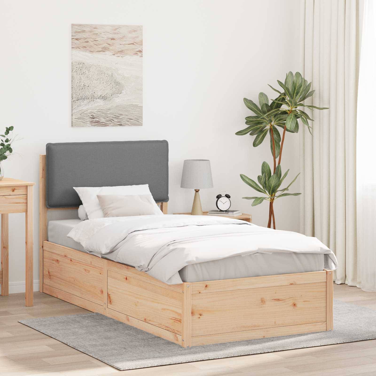 Ein ordentlich gemachtes Doppelbett mit einem grauen Kopfteil, in einem hellen Raum mit einer Topfpflanze, einer Lampe und einem gerahmten Kunstwerk an der Wand.