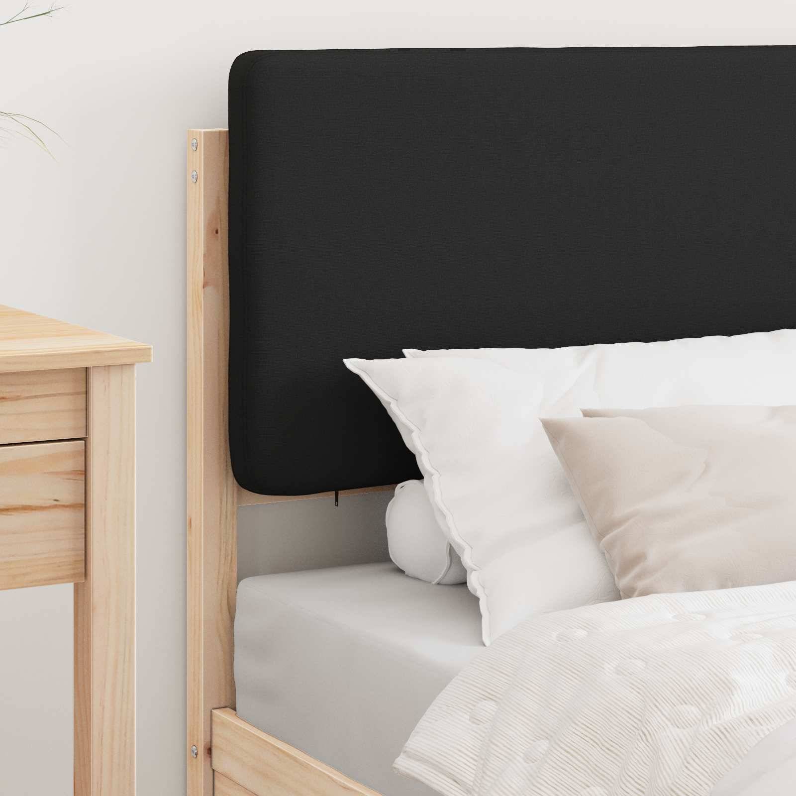 Ein ordentlich gemachtes Bett mit einem schwarzen Kopfteil, weißen und beigen Kissen und einem hellen Holzrahmen. Ein Holznachttisch ist teilweise zu sehen.