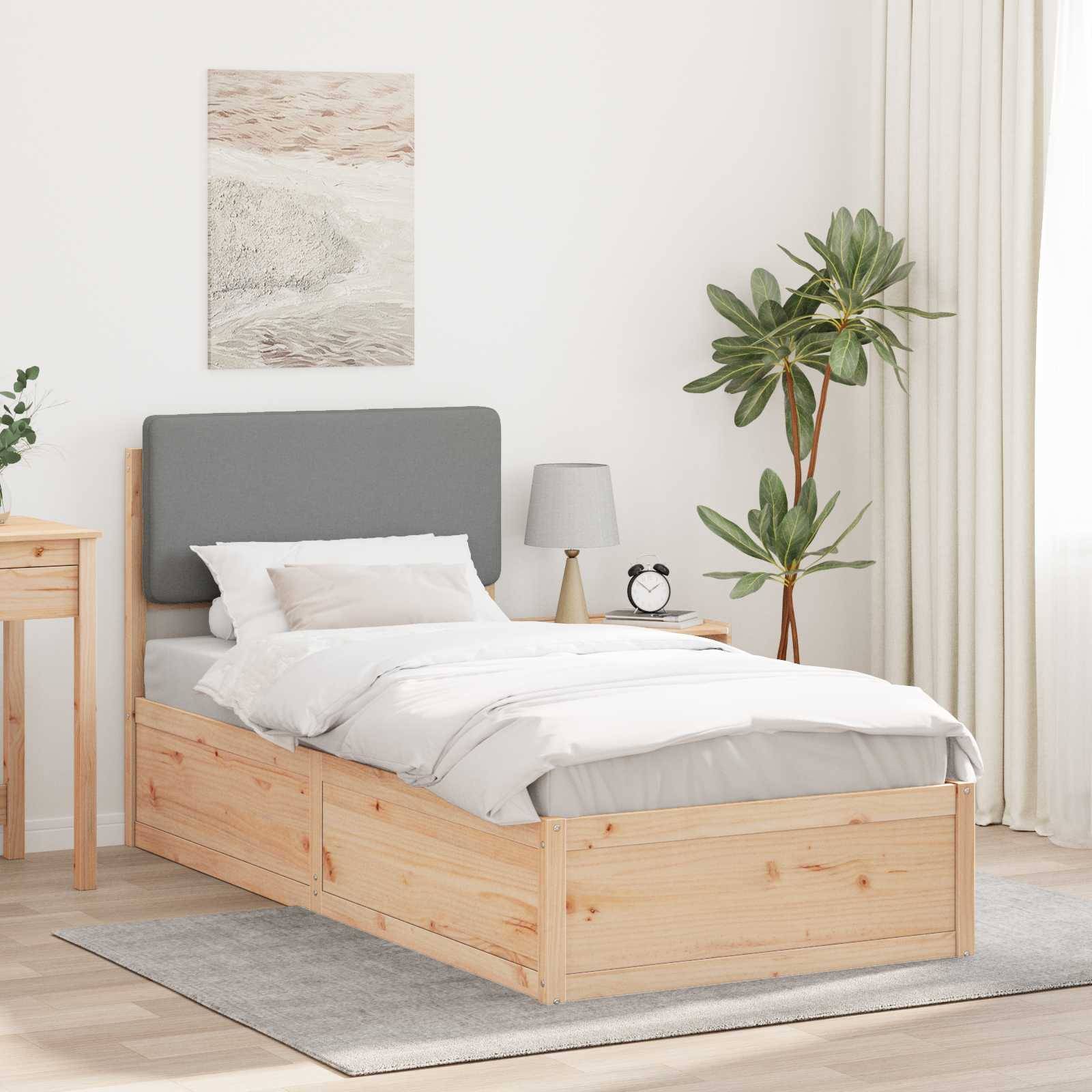 Ein aufgeräumtes Schlafzimmer mit einem Holzbett, grauem Kopfteil, weißer Bettwäsche, einer Pflanze, einem Nachttisch mit Lampe und neutraler Wanddekoration.