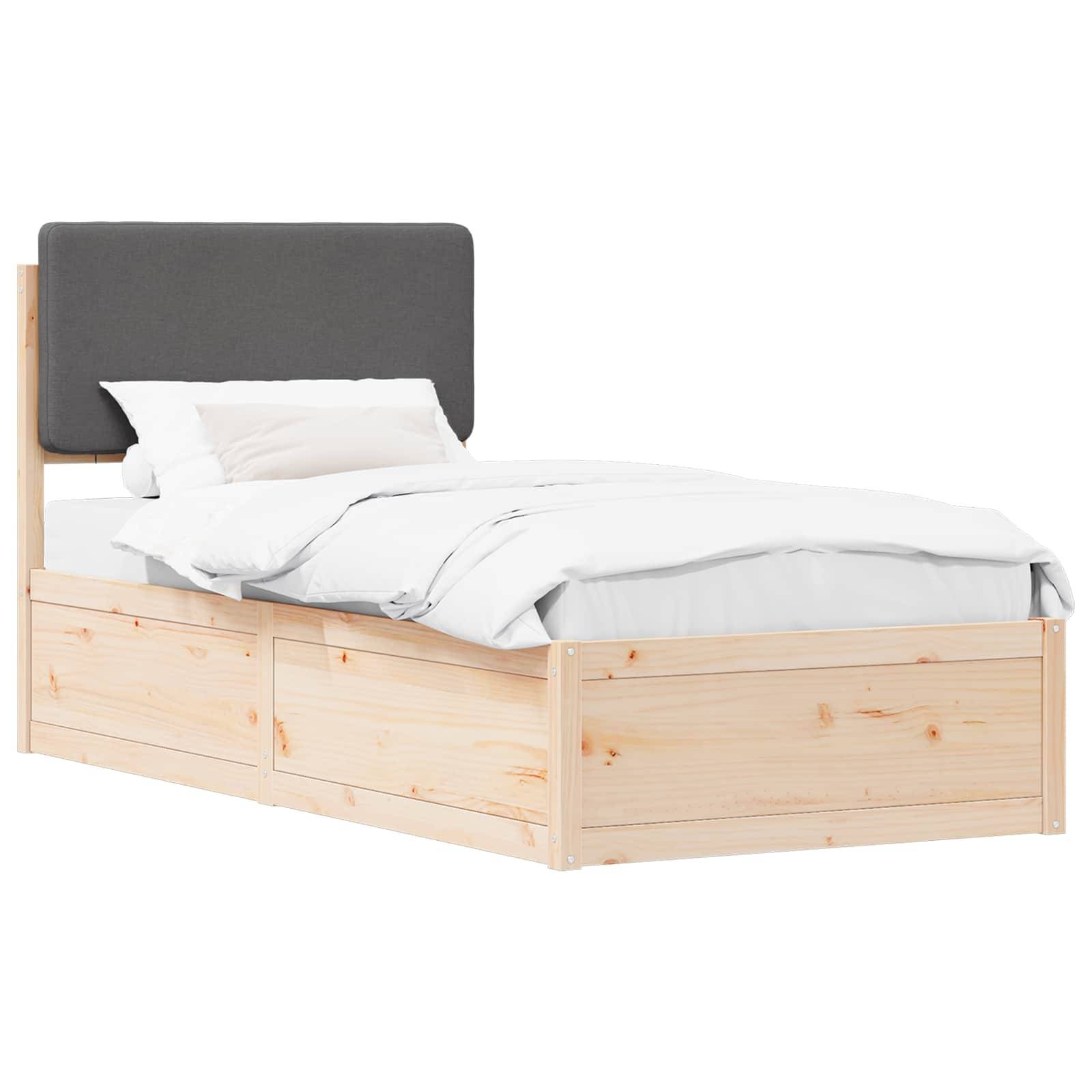 Ein Holzbettgestell mit gepolstertem grauem Kopfteil, weißer Bettwäsche und Kissen, von der Seite aufgenommen.