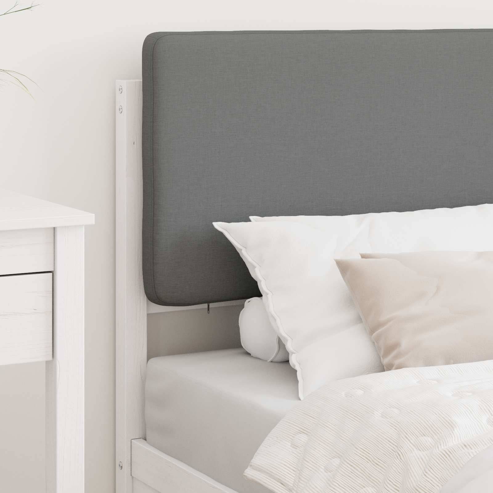 Ein ordentlich gemachtes Bett mit weißen und beigen Kissen, versehen mit einem grauen gepolsterten Kopfteil, neben einem weißen Nachttisch.