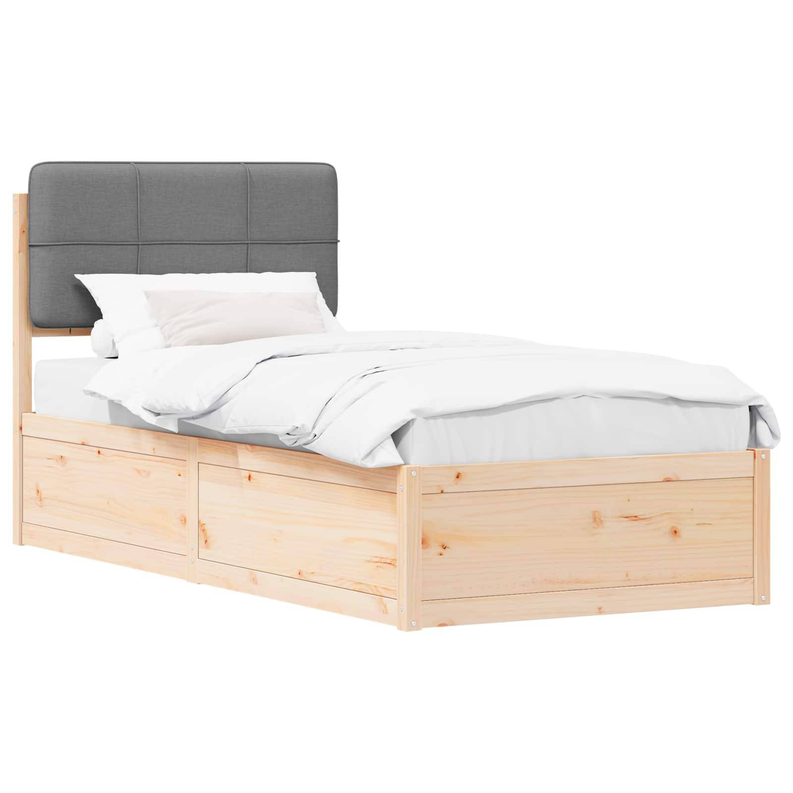 Ein Holz-Einzelbett mit einem grauen gepolsterten Kopfteil, weißer Bettwäsche und einem einzelnen Kissen, von schräg gesehen.
