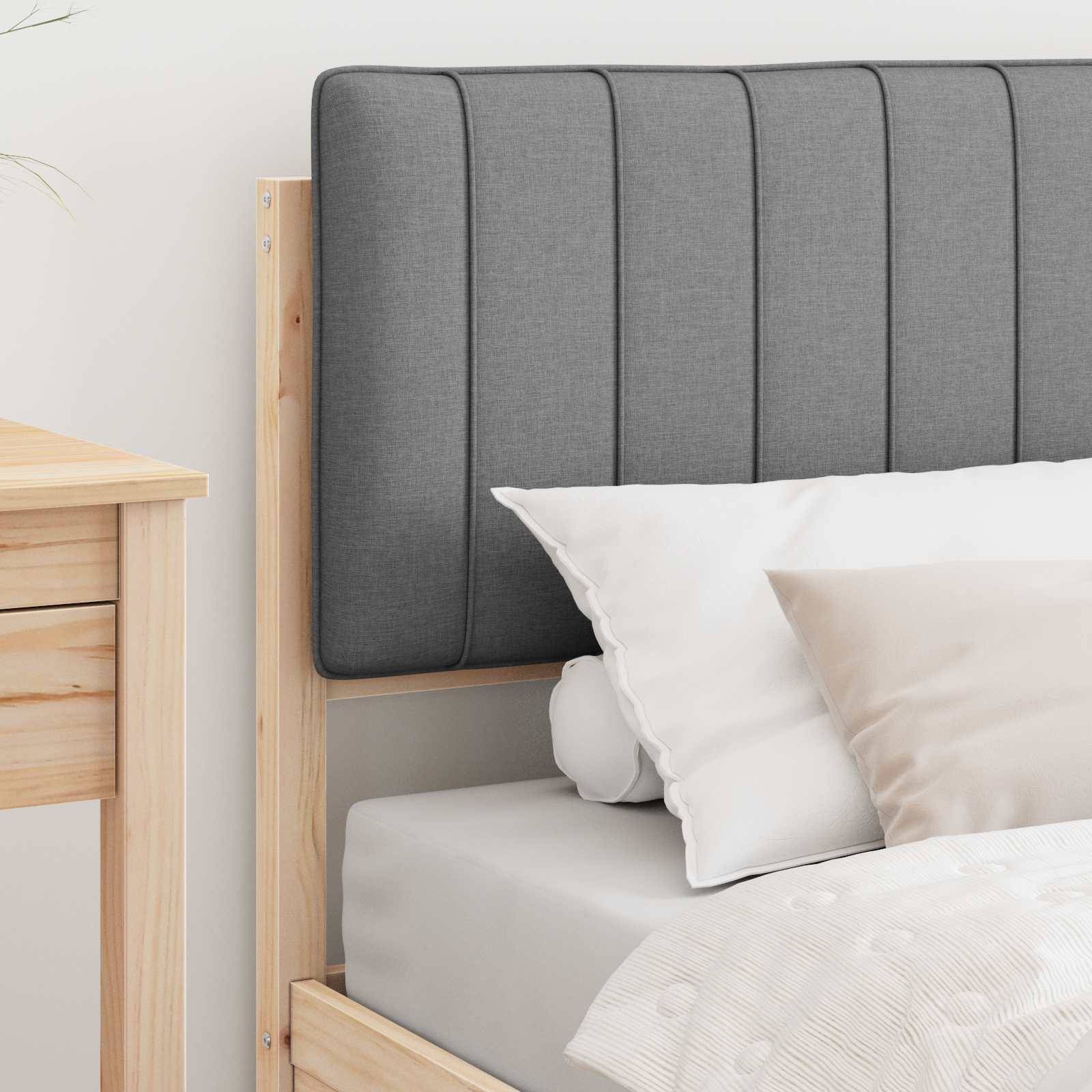 Ein ordentlich gemachtes Bett mit grauem gepolstertem Kopfteil und beigen Dekorationskissen in einem Rahmen aus hellem Holz, neben einem hölzernen Nachttisch.
