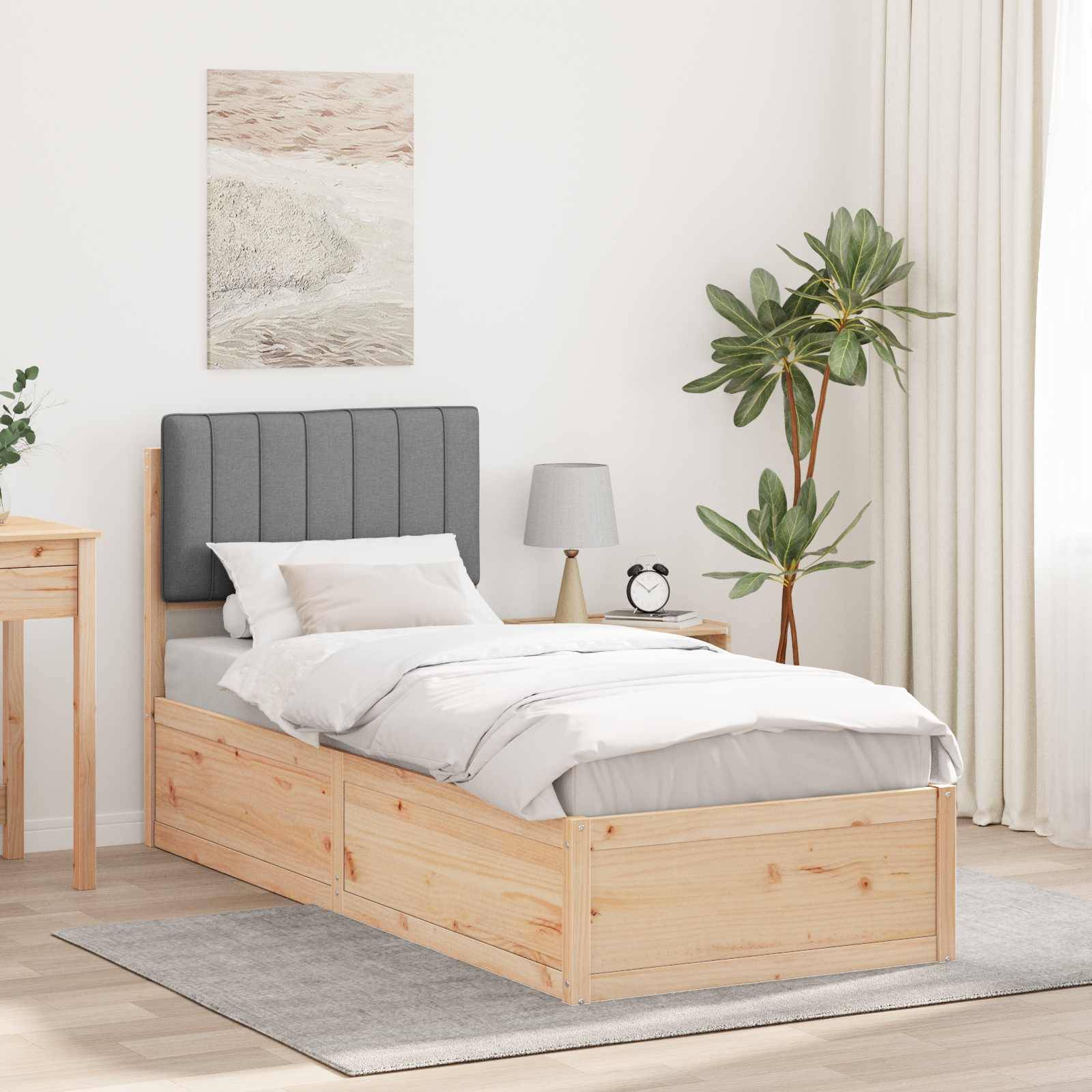 Ein gut beleuchtetes Schlafzimmer mit einem Holzbett, einem grauen Kopfteil, weißer Bettwäsche, einem kleinen Nachttisch mit einer Lampe und einer Topfpflanze.