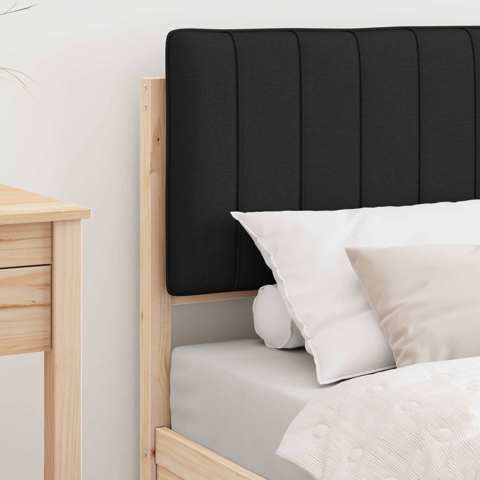 Ein ordentlich gemachtes Bett mit einem Holzrahmen ist zu sehen. Das Bett hat weiße und beige Kissen und einen dunklen gepolsterten Kopfteil. Daneben steht ein Holznachttisch.