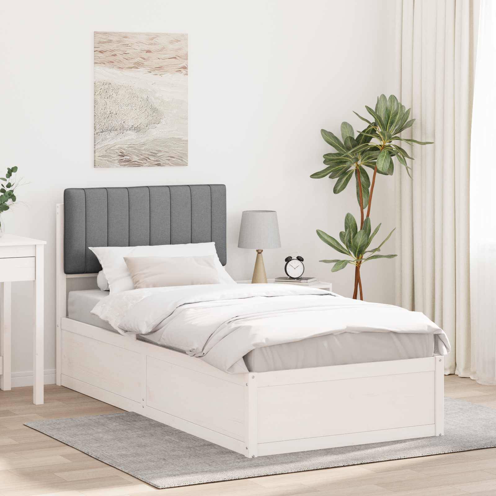 Ein modernes Schlafzimmer zeigt ein ordentlich gemachtes Bett mit grauem Kopfteil, weißer Bettwäsche, zwei Kissen, einem Nachttisch mit einer Lampe und einer Uhr, einer Pflanze und einem Wandkunstwerk darüber.