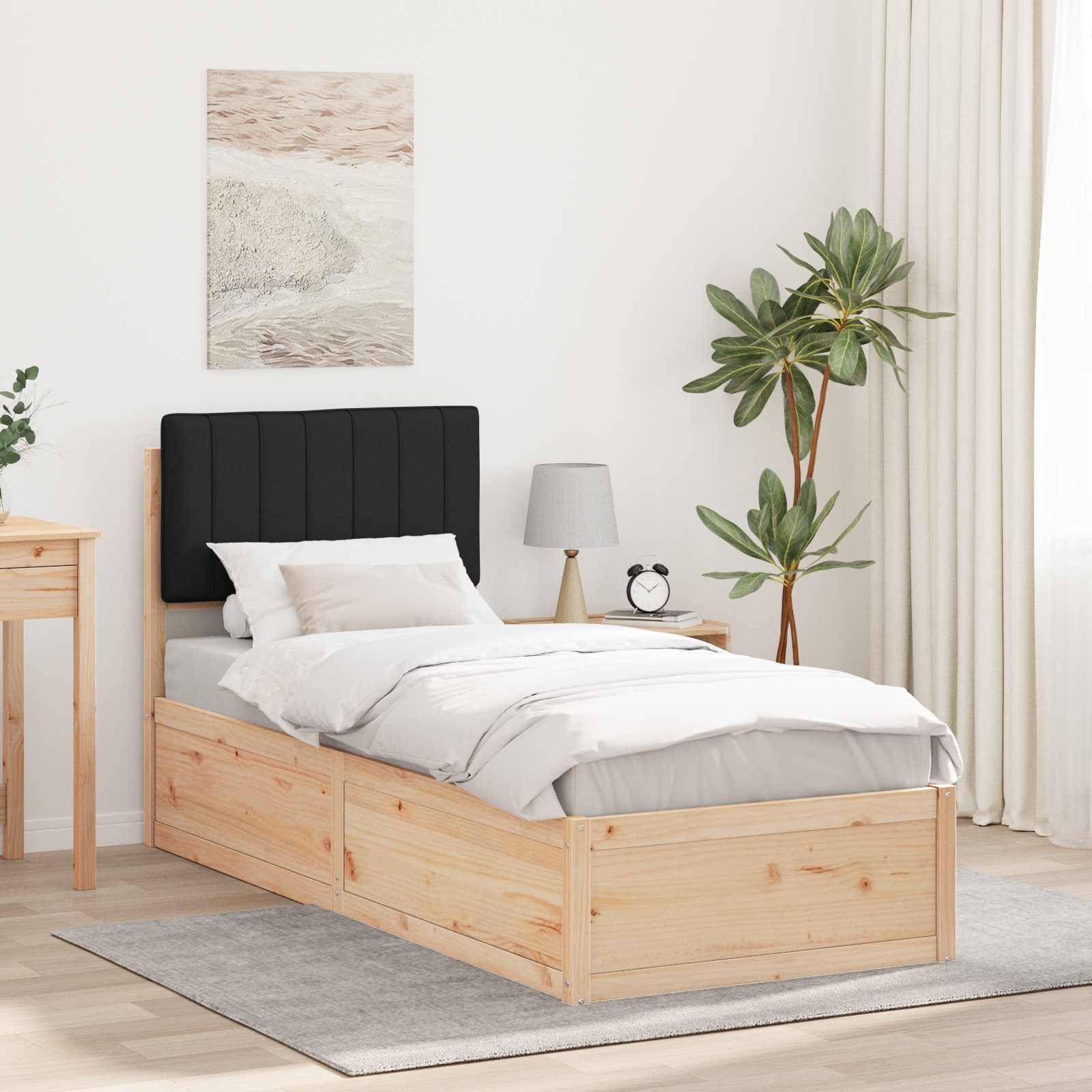 Ein gemütliches Schlafzimmer zeigt ein Holzbett mit grauer Bettwäsche, einem schwarzen Kopfteil, einem kleinen Nachttisch mit einer Lampe und einer Pflanze am Fenster.