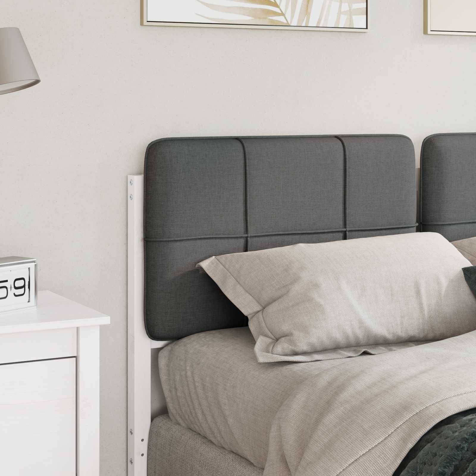 Ein ordentlich gemachtes Bett mit einem grauen gepolsterten Kopfteil steht neben einem weißen Nachttisch. Der Raum ist minimalistisch mit leichter Dekoration.
