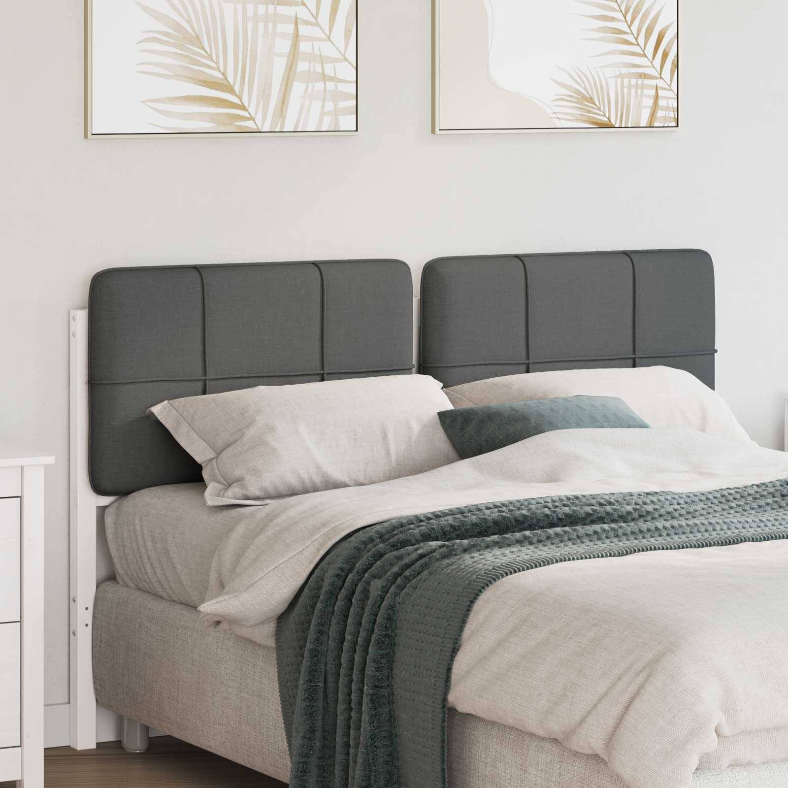 Ein sauber gemachtes Bett mit grau-weißer Bettwäsche, zwei quadratischen Kissen und einer strukturierten Decke, vor einer hellen Wand mit dekorativen Rahmen.