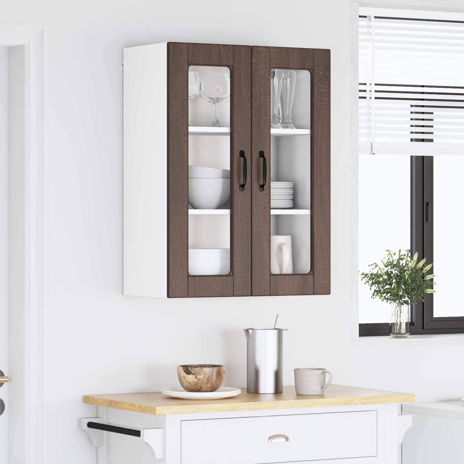Eine Küchenszene mit weißen und dunkelholzfarbenen Wandschränken, in denen Gläser ausgestellt sind, Teller auf einer Arbeitsplatte, eine kleine Pflanze und ein Fenster.