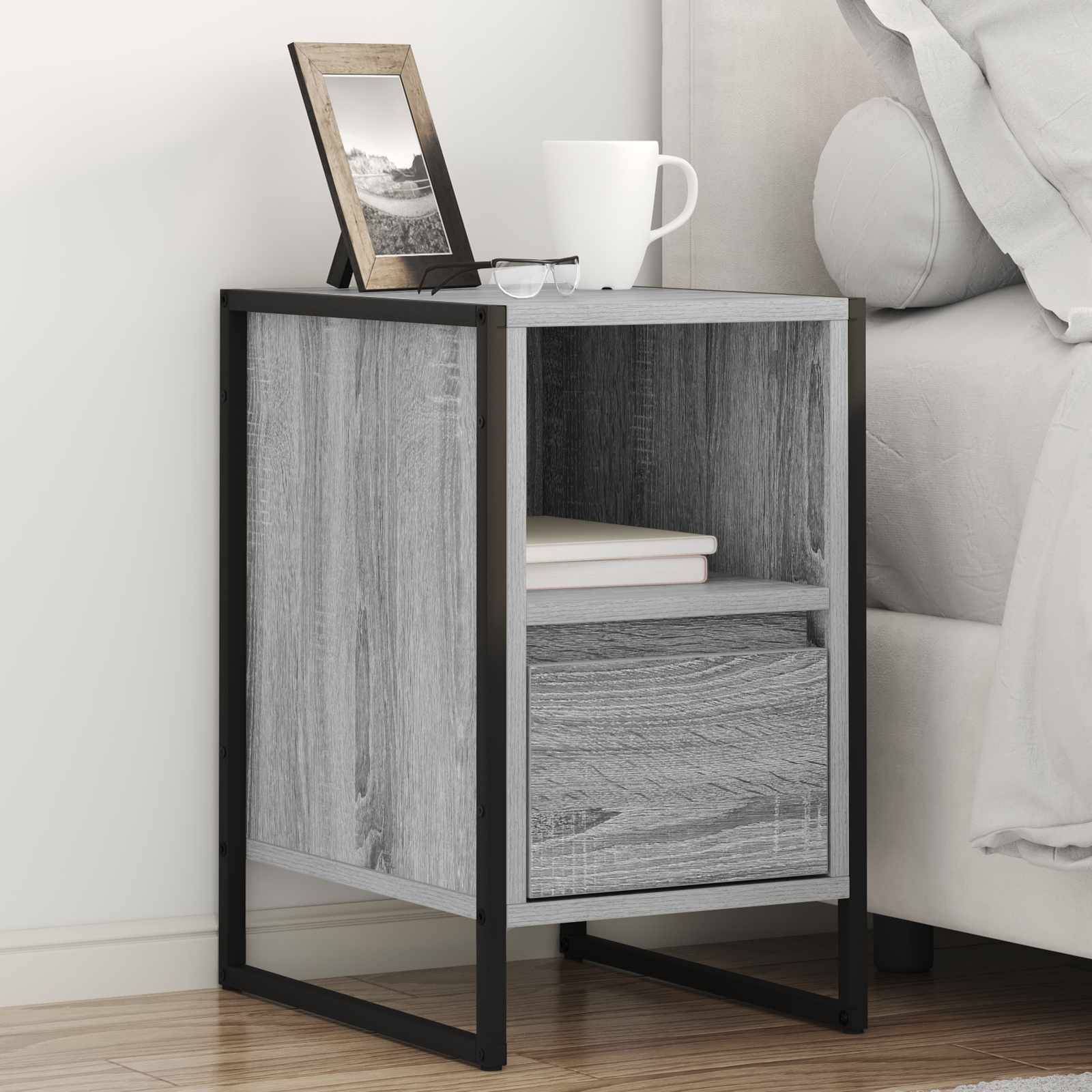 Ein kleiner Nachttisch mit Holz- und Metalldesign, auf dem ein Fotorahmen, eine weiße Tasse und Bücher stehen, befindet sich neben einem Bett mit weißer Bettwäsche.
