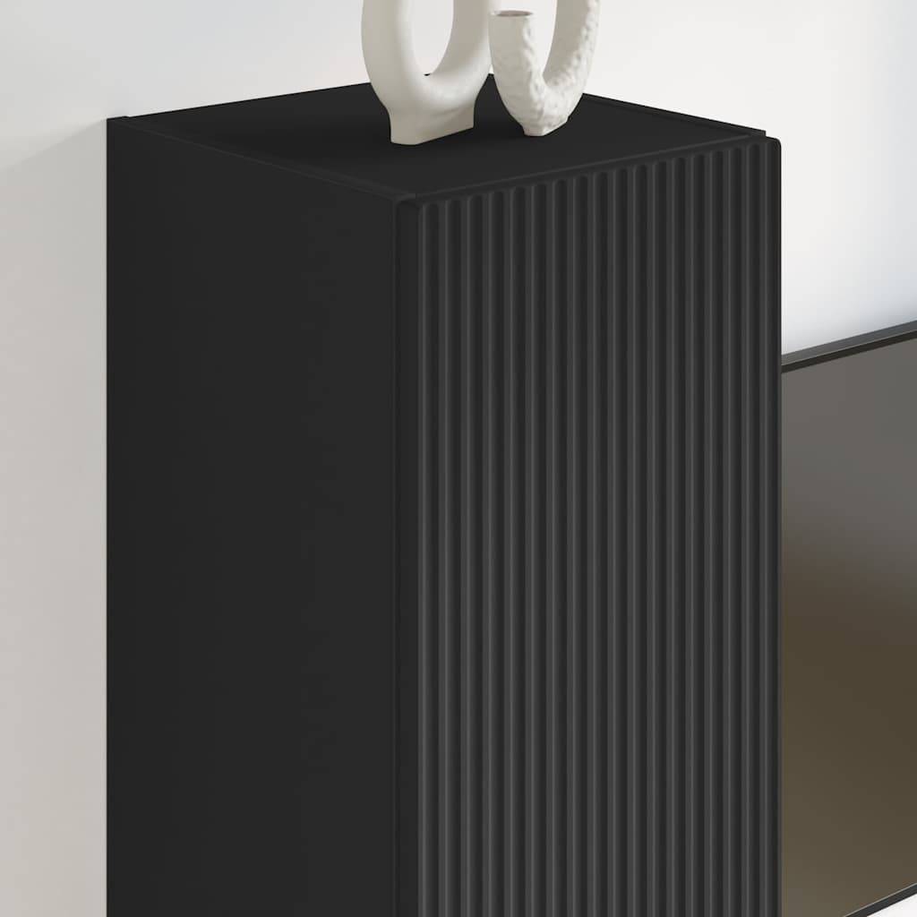 Ein hoher, schwarzer, rechteckiger Schrank mit vertikalen Rillen, gekrönt von einem dekorativen geschwungenen Objekt vor einer weißen Wand.