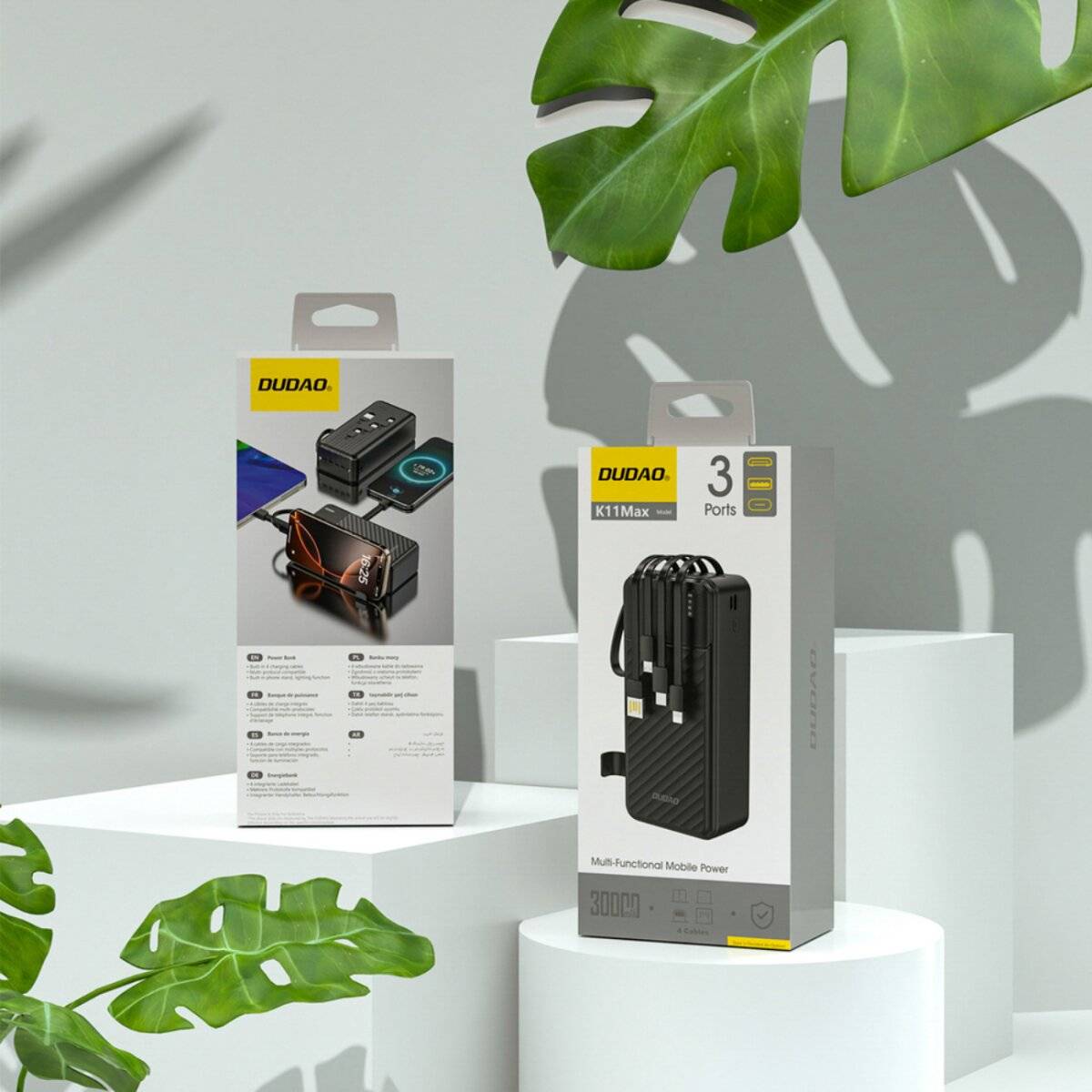 Zwei elektronische Geräteverpackungskartons, mit 'DUDAO' beschriftet, auf weißen Podesten platziert, umgeben von grünen Blättern.