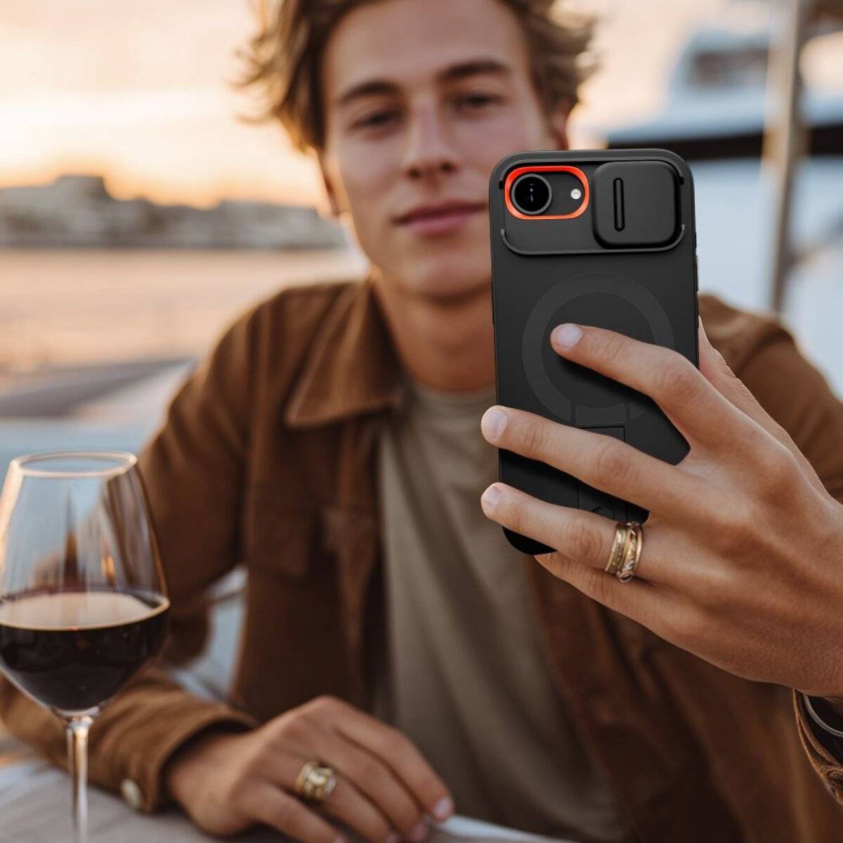 Eine Person, die sich an einem Außencafé mit einem Smartphone ein Selfie macht, mit einem Glas Rotwein auf dem Tisch und einem unscharfen Hintergrund.