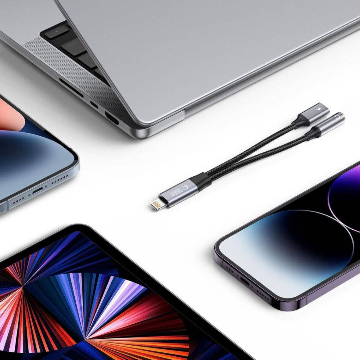 Eine Flachaufnahme moderner Technikgeräte: ein Laptop, Smartphone und Tablet, angeordnet mit einem schwarzen geflochtenen USB-Kabel in minimalem Stil.