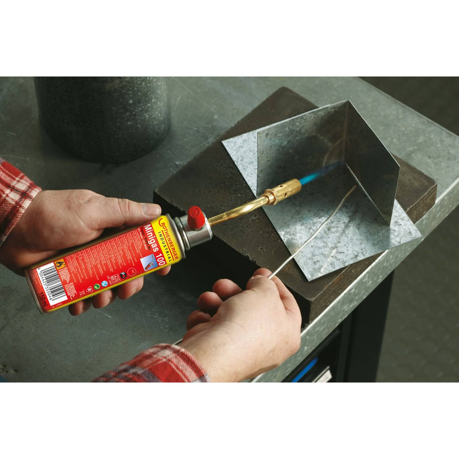 Eine Person verwendet einen Gasbrenner, um Metallteile auf einer Werkbank zu verbinden und dabei einen Schweißprozess zu demonstrieren.