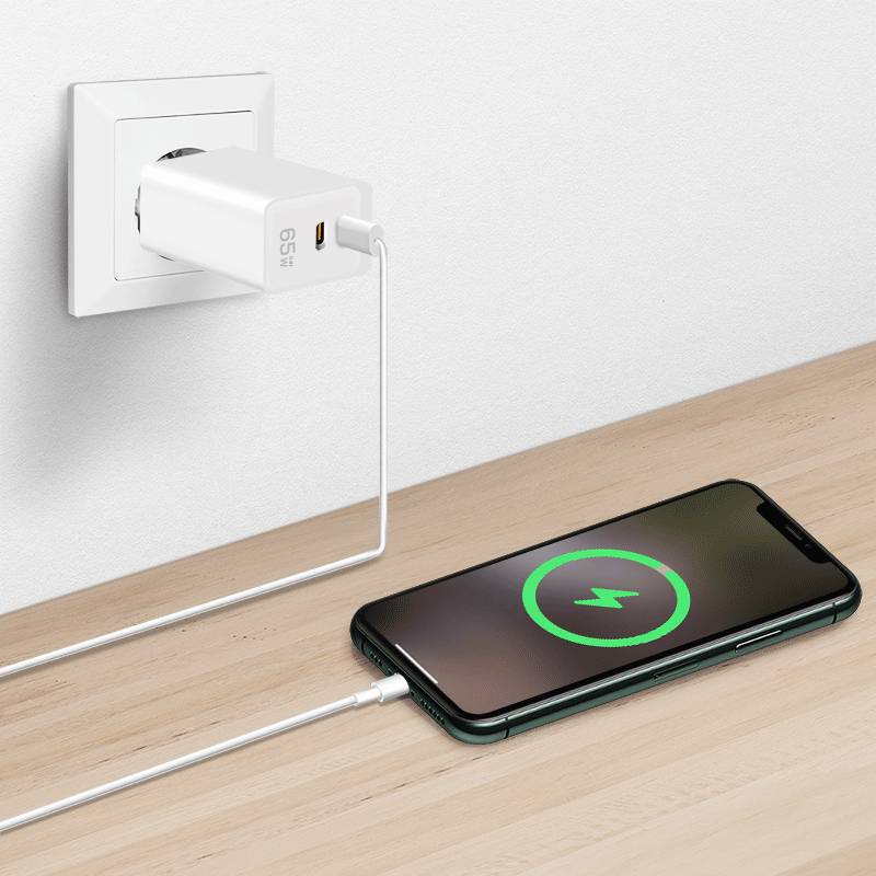 Ein Smartphone, das auf einem Holztisch lädt. Ein weißes Ladekabel verbindet das Telefon mit einem Wandsteckdosenadapter. Auf dem Bildschirm des Telefons wird ein Ladeicon angezeigt.