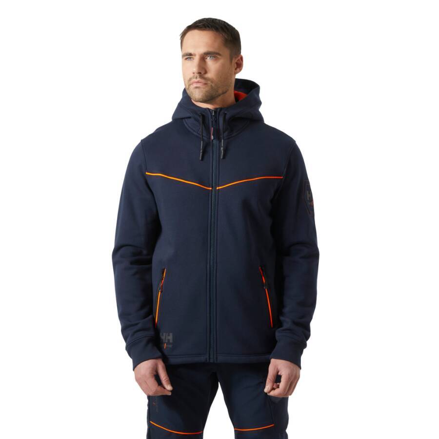 Ein Mann trägt einen marineblauen Zip-Hoodie mit orangefarbenen Akzenten und passender Hose. Er blickt zur Seite, die Hände in den Taschen, vor einem einfarbigen Hintergrund.