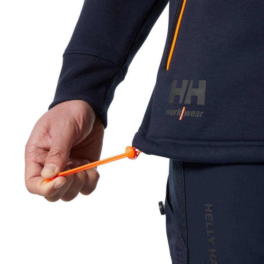 Eine Person justiert den Kordelzug einer marineblauen Helly Hansen Jacke und zeigt dabei eine Nahaufnahme des Markenlogos und der Bekleidungsdetails.