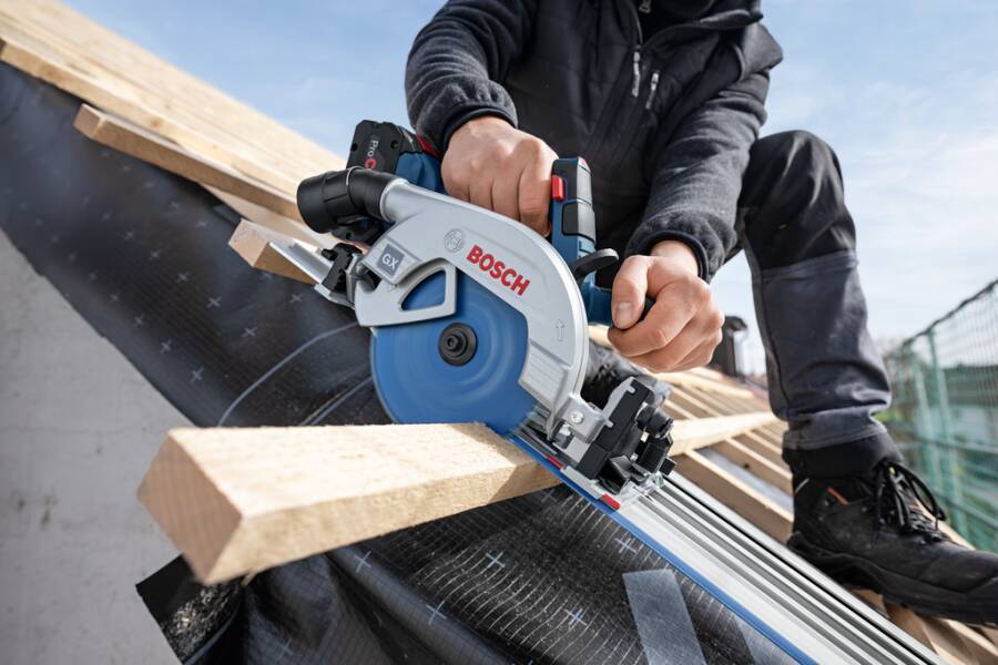 Eine Person, die eine Bosch-Kreissäge verwendet, um Holzbretter auf einem geneigten Dach zu schneiden, mit Fokus auf das Werkzeug und die Hände für präzise Arbeit.