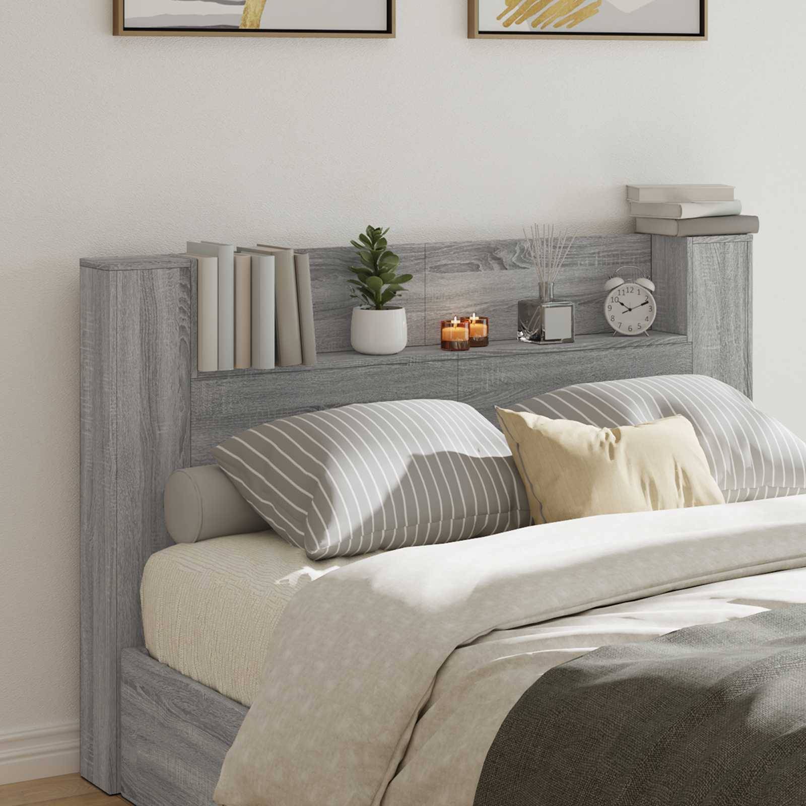 Ein ordentlich gemachtes Bett mit gestreiften Kissen und einem beigen Kissen, flankiert von einem grauen Kopfteil mit Büchern, einer Pflanze und Kerzen darauf.