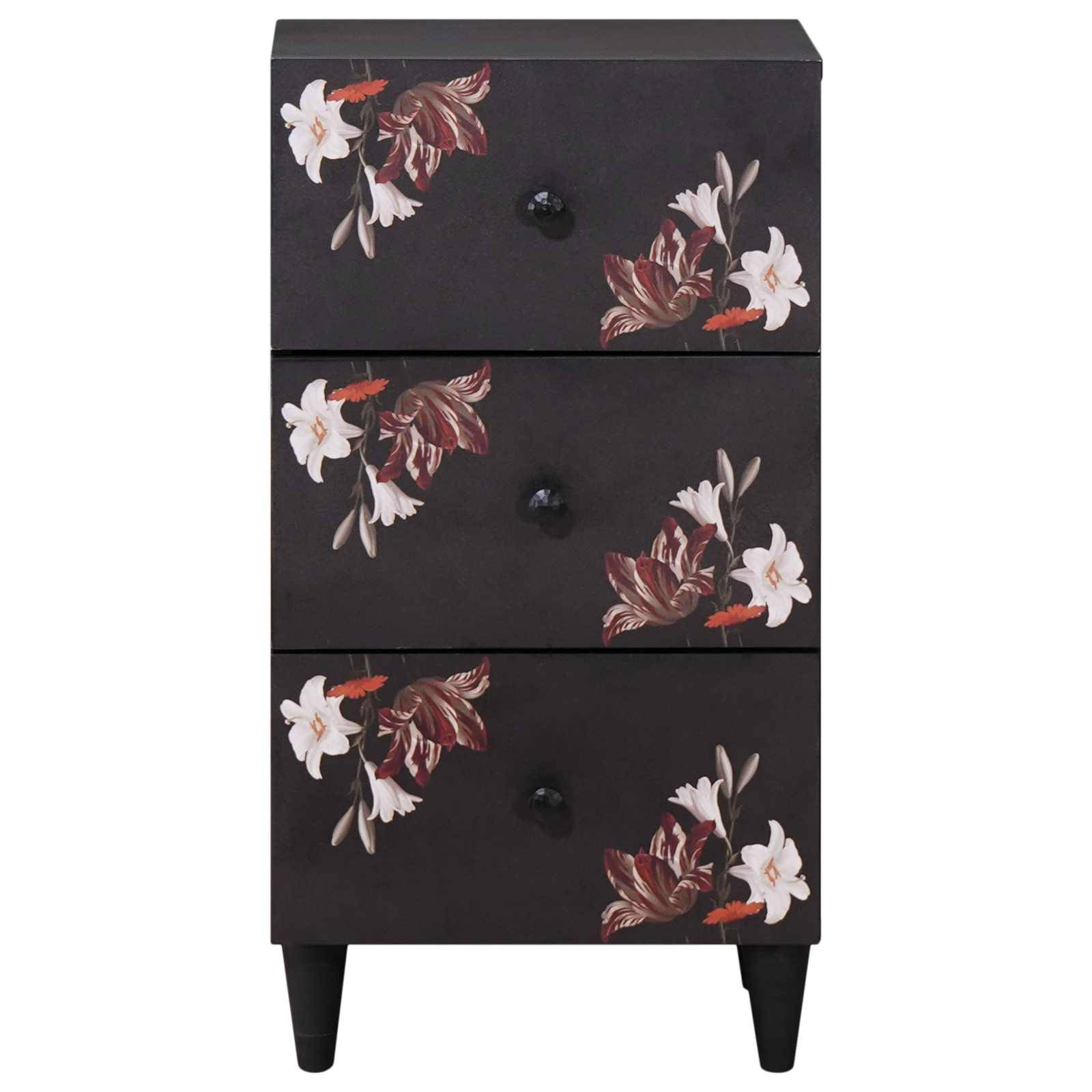 Eine schwarze Kommode mit drei Schubladen, auf deren Frontseiten jeweils florale Muster in Weiß und Rot zu sehen sind. Die Kommode steht auf kurzen schwarzen Beinen.