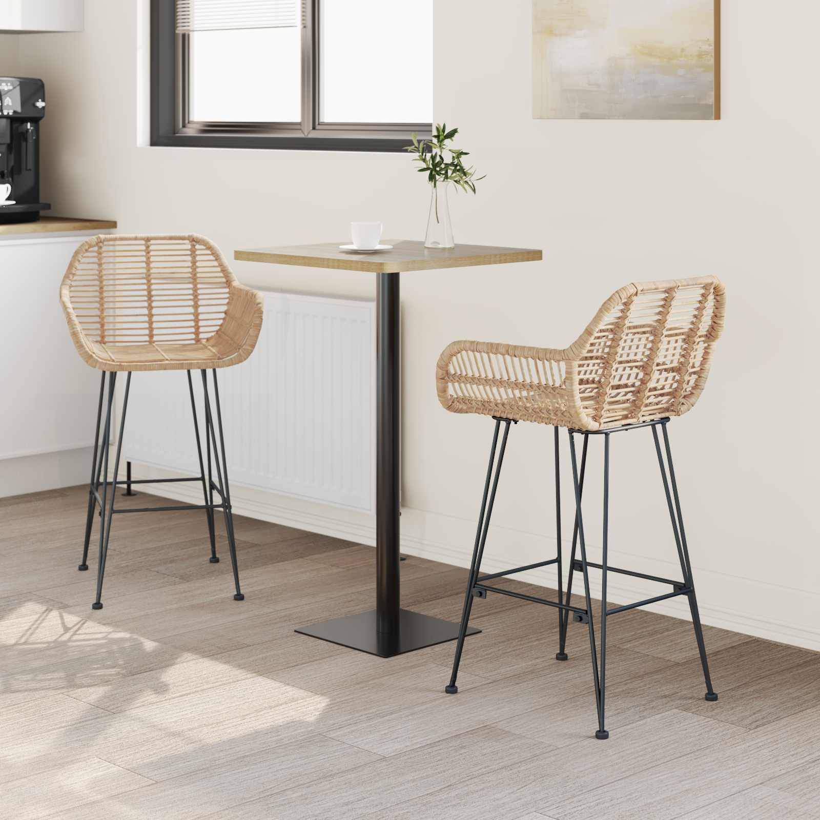 Gemütliche Küchenecke mit einem kleinen quadratischen Holztisch und zwei Korbhockern auf hohen schwarzen Gestellen. Eine Topfpflanze und abstrakte Wandkunst ergänzen die Dekoration.