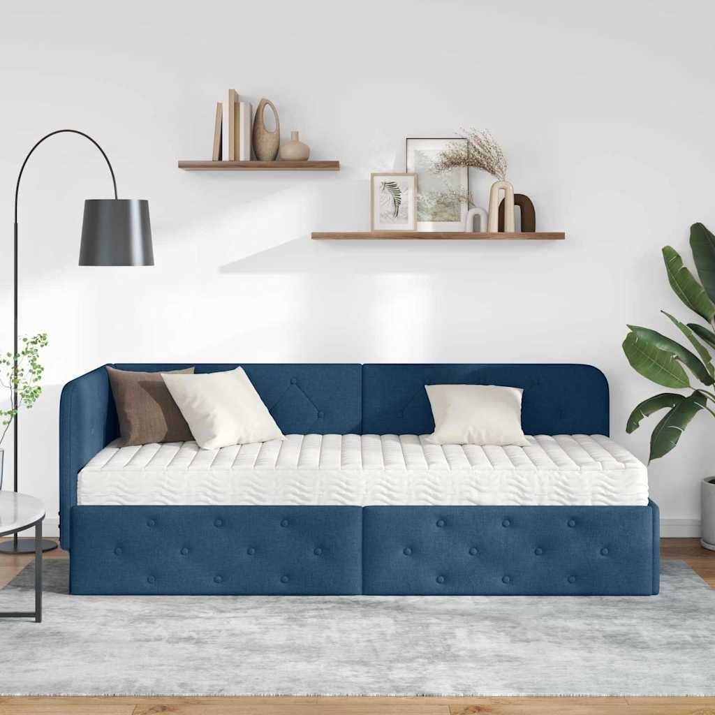Ein modernes Wohnzimmer zeigt ein blaues Sofa mit geometrischem Muster, weiße Kissen, eine Stehlampe, Holzregale und Zimmerpflanzen.
