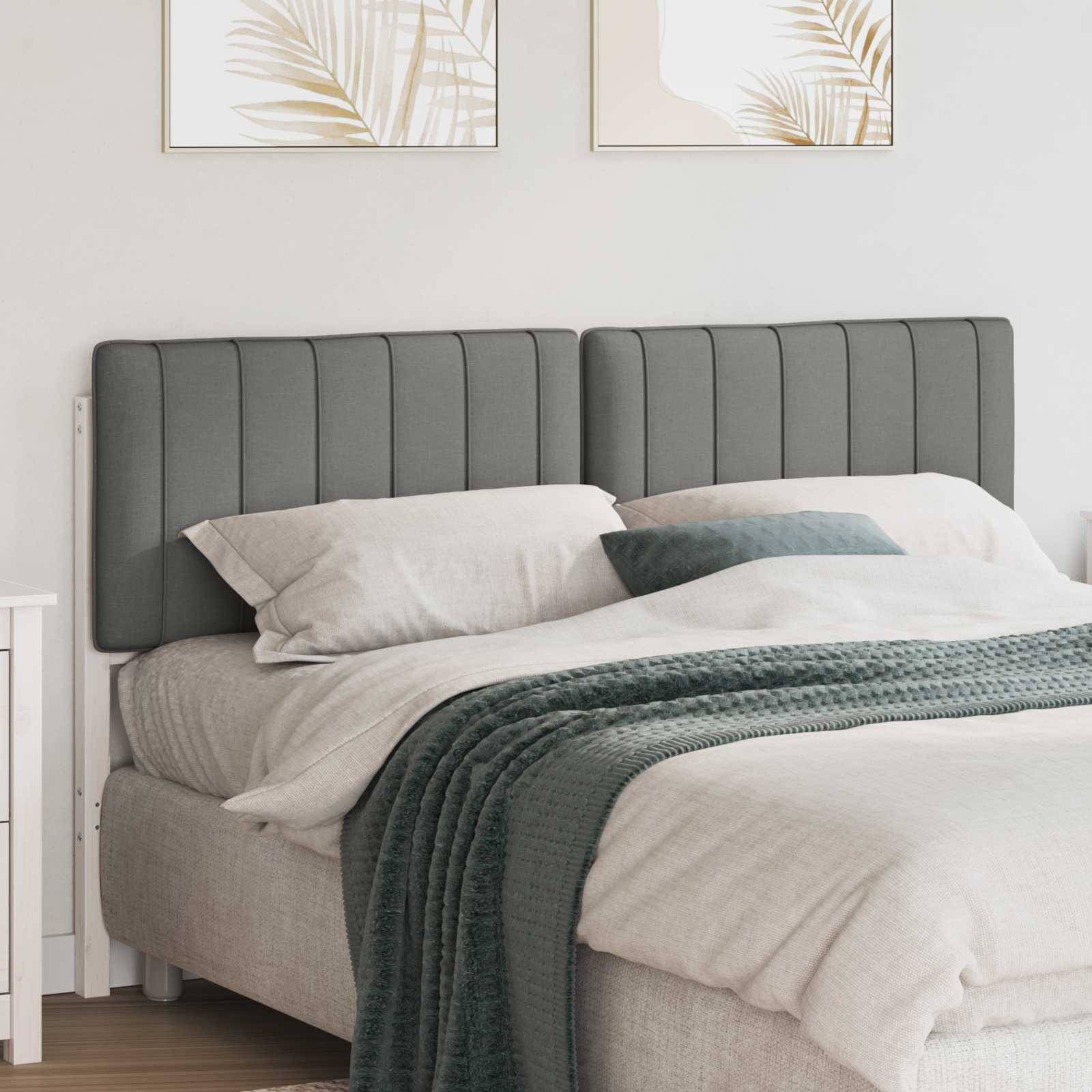 Ein ordentlich gemachtes Bett mit grau gepolstertem Kopfteil, weißen Laken und einer grünen gestrickten Decke. Zwei gerahmte Blätterdrucke hängen darüber.