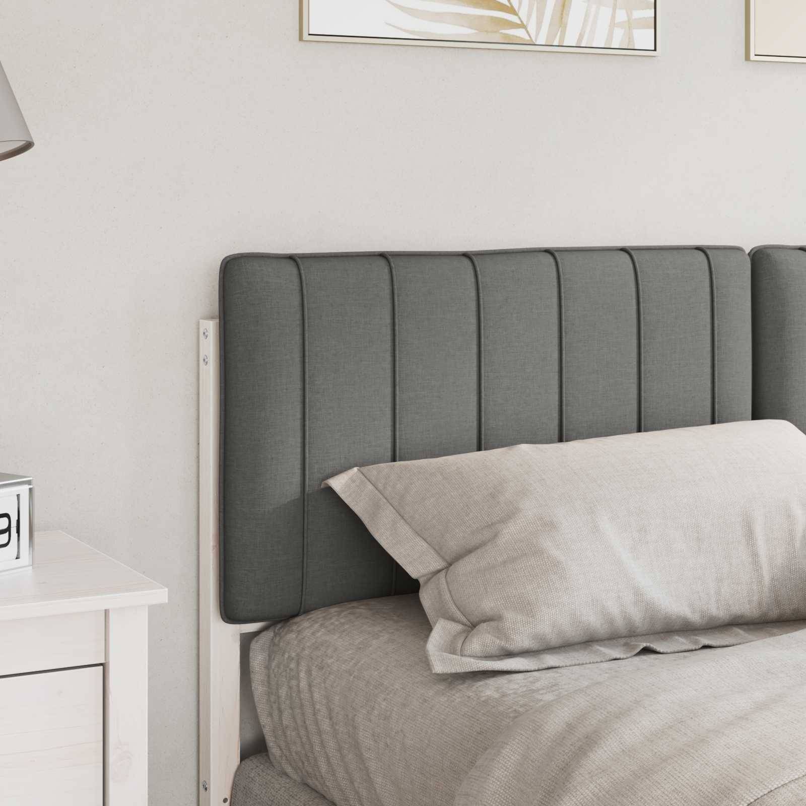 Ein sorgfältig gemachtes Bett mit einem grauen, gepolsterten Kopfteil vor einer hellgefärbten Wand. Ein weißer Nachttisch ist teilweise daneben sichtbar.