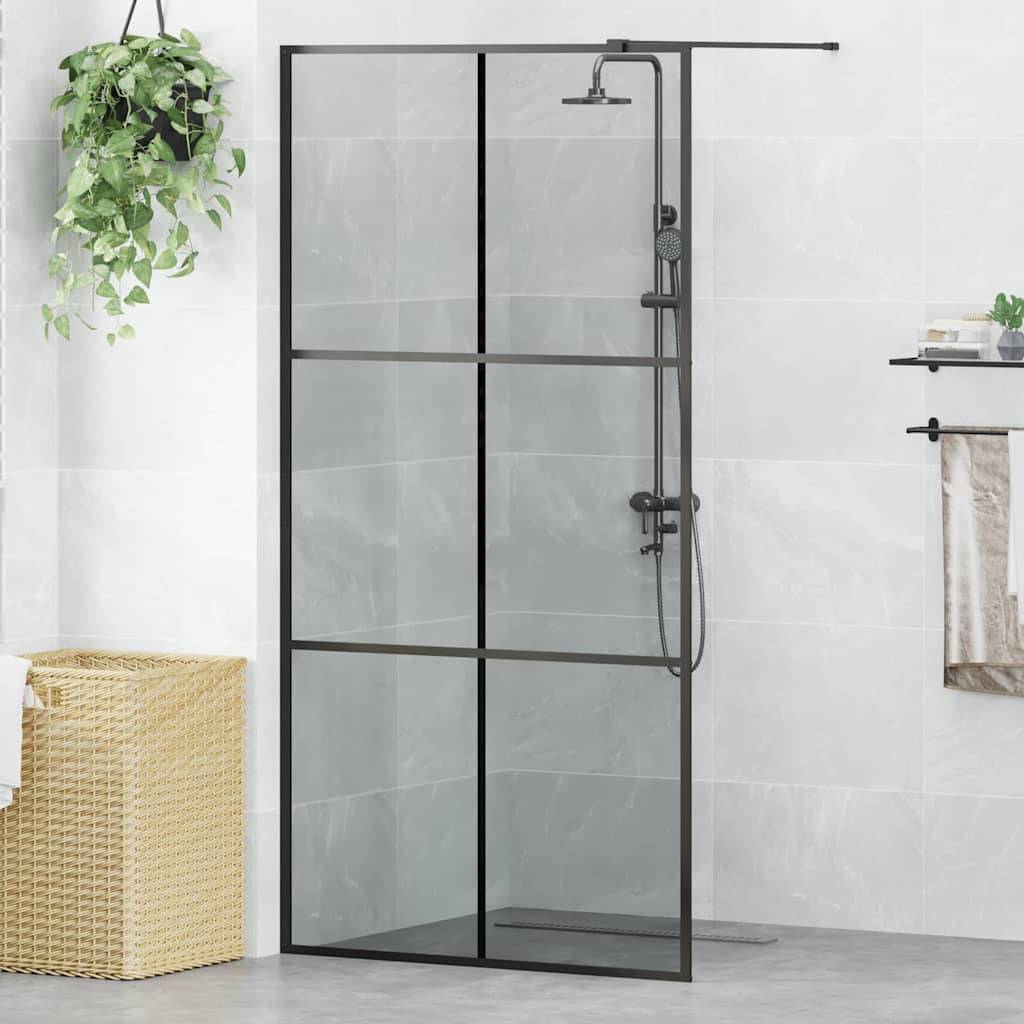 Ein modernes Badezimmer mit einer Dusche mit Glaswand, schwarzen Armaturen, einer hängenden Pflanze und einem Weidenkorb auf einem gefliesten Boden.