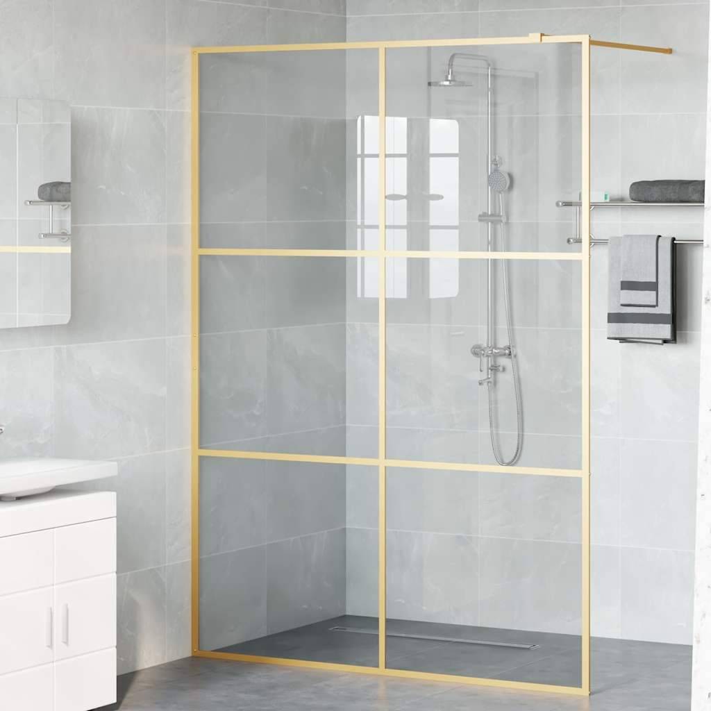 Ein modernes Badezimmer mit einer Duscheinfassung aus Glas mit goldenem Rahmen, einer Regendusche und grauen Fliesen. Ein weißes Waschbecken und zusammengefaltet Handtücher sind zu sehen.
