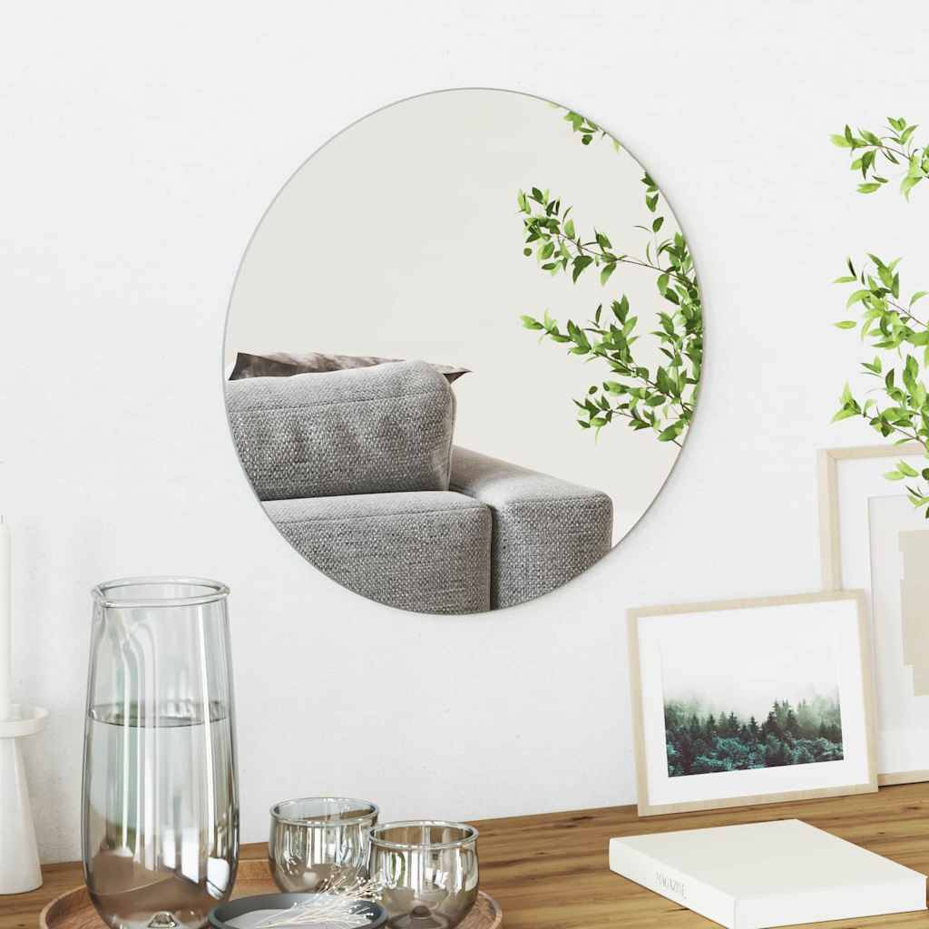 Ein rundes Spiegel an der Wand reflektiert einen Teil eines grauen Sofas und grüner Pflanzen. Auf dem Tisch darunter befinden sich ein Glas, eine Kerze und ein gerahmtes Gemälde.