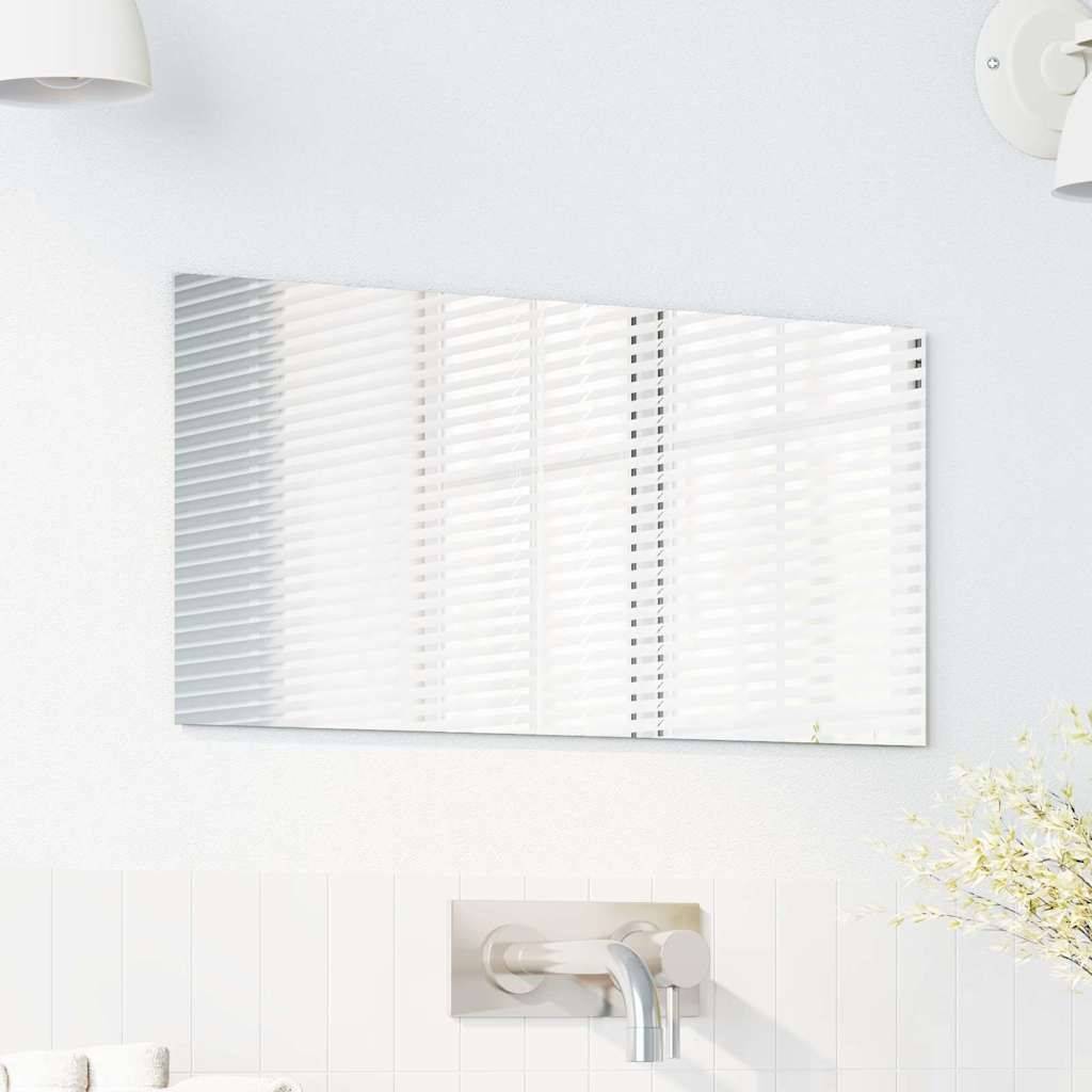 Eine weiße Badezimmerwand zeigt einen horizontal montierten Spiegel, der ein Fenster mit geschlossenen Jalousien reflektiert. Unterhalb des Spiegels ist ein Metallwasserhahn sichtbar.