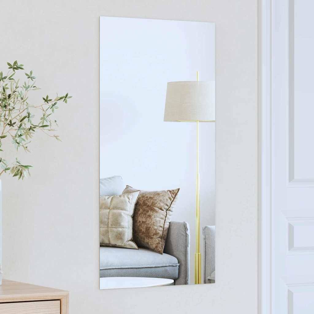 Ein Spiegelbild an einer Wandreflexion zeigt ein gemütliches Wohnzimmer mit einem hellgrauen Sofa, mehreren braunen Kissen und einer hohen Stehlampe.