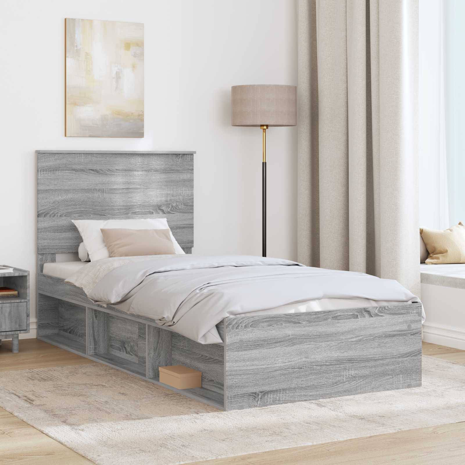 Ein minimalistisches Schlafzimmer zeigt ein graues Holzbett mit Stauraum, einen passenden Nachttisch, eine beige Lampe und einen Fensterplatz mit Vorhängen.