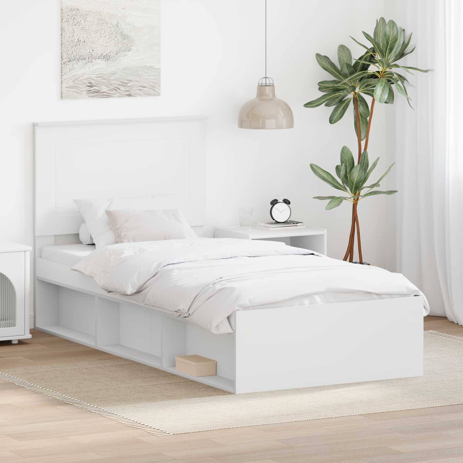 Ein modernes Schlafzimmer zeigt ein weißes Bett mit Schubladen, flankiert von einem Nachttisch und einer belaubten Pflanze. Sanftes Licht schafft eine gemütliche Atmosphäre.