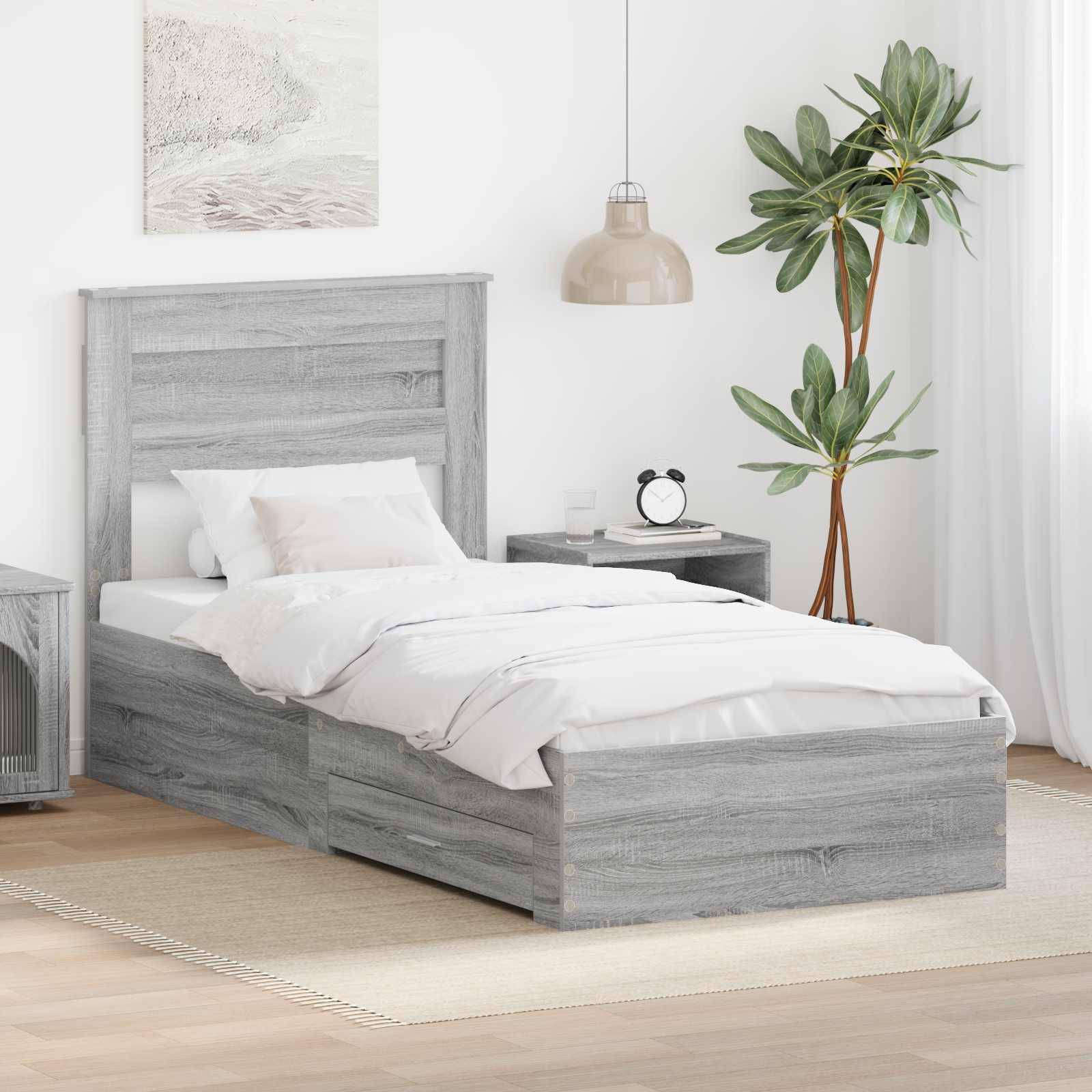 Ein modernes Schlafzimmer zeigt ein graues Holzbett mit weißer Bettwäsche, zwei passenden Nachttischen, einem Gemälde an der Wand und einer hohen, belaubten Pflanze.