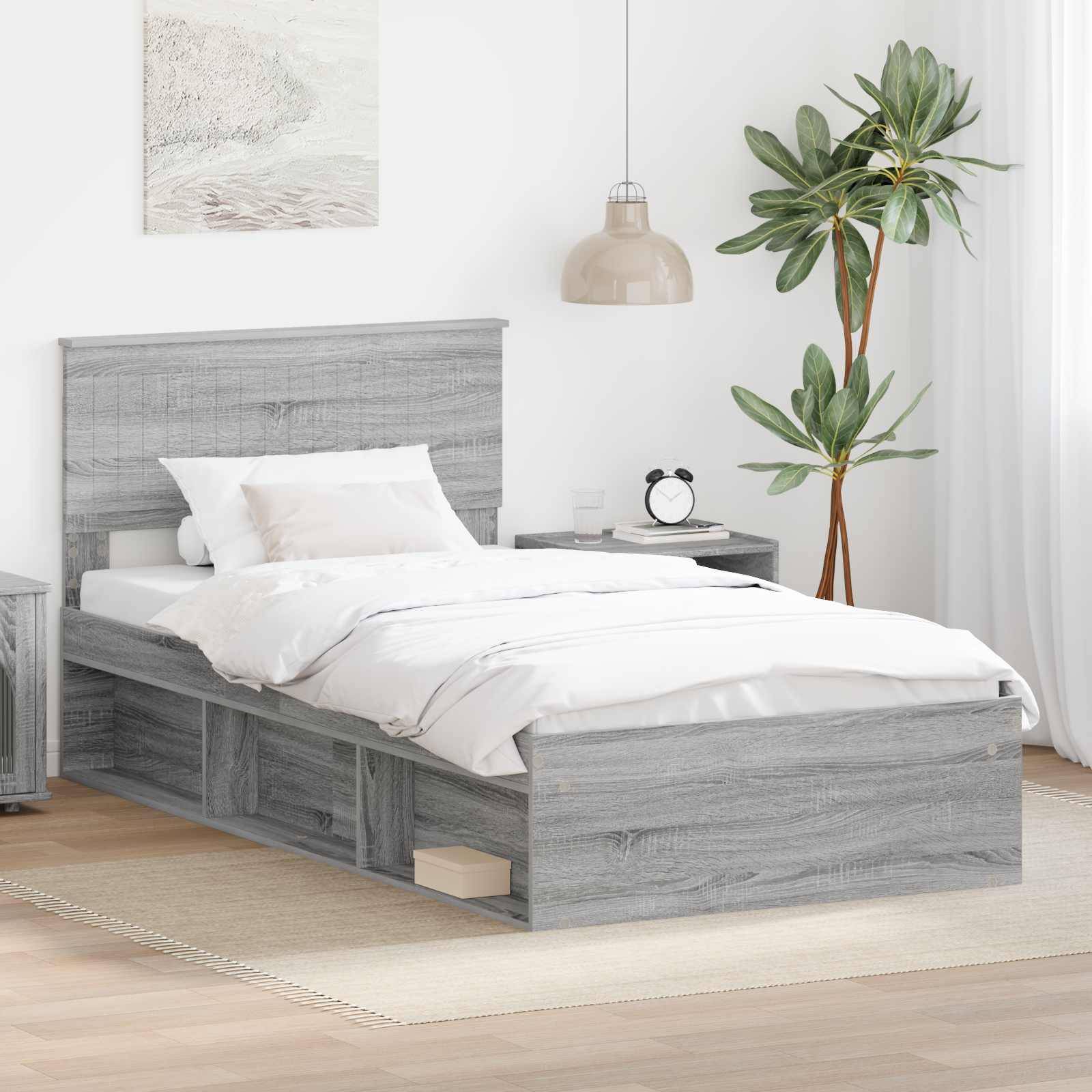 Ein modernes Schlafzimmer mit einem grauen Holzbett, weißer Bettwäsche, einem Nachttisch mit Lampe und Uhr sowie einer großen grünen Pflanze in der Ecke.
