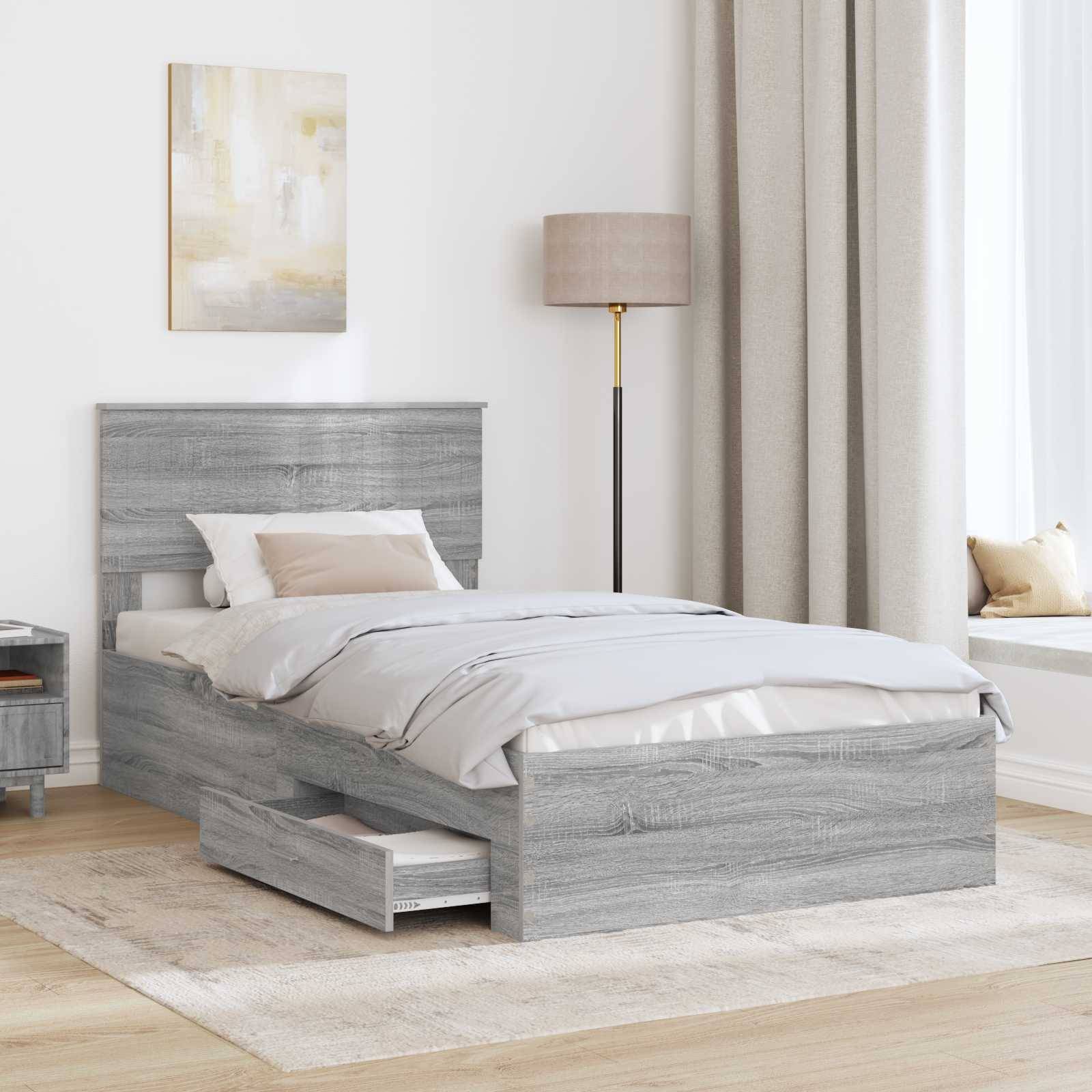 Ein ordentlich gemachtes Bett mit grauem Holzrahmen und Schubladenspeicher, neben einer Stehlampe, in einem hell getönten Schlafzimmer mit Wandkunst und einer Fensterbank.
