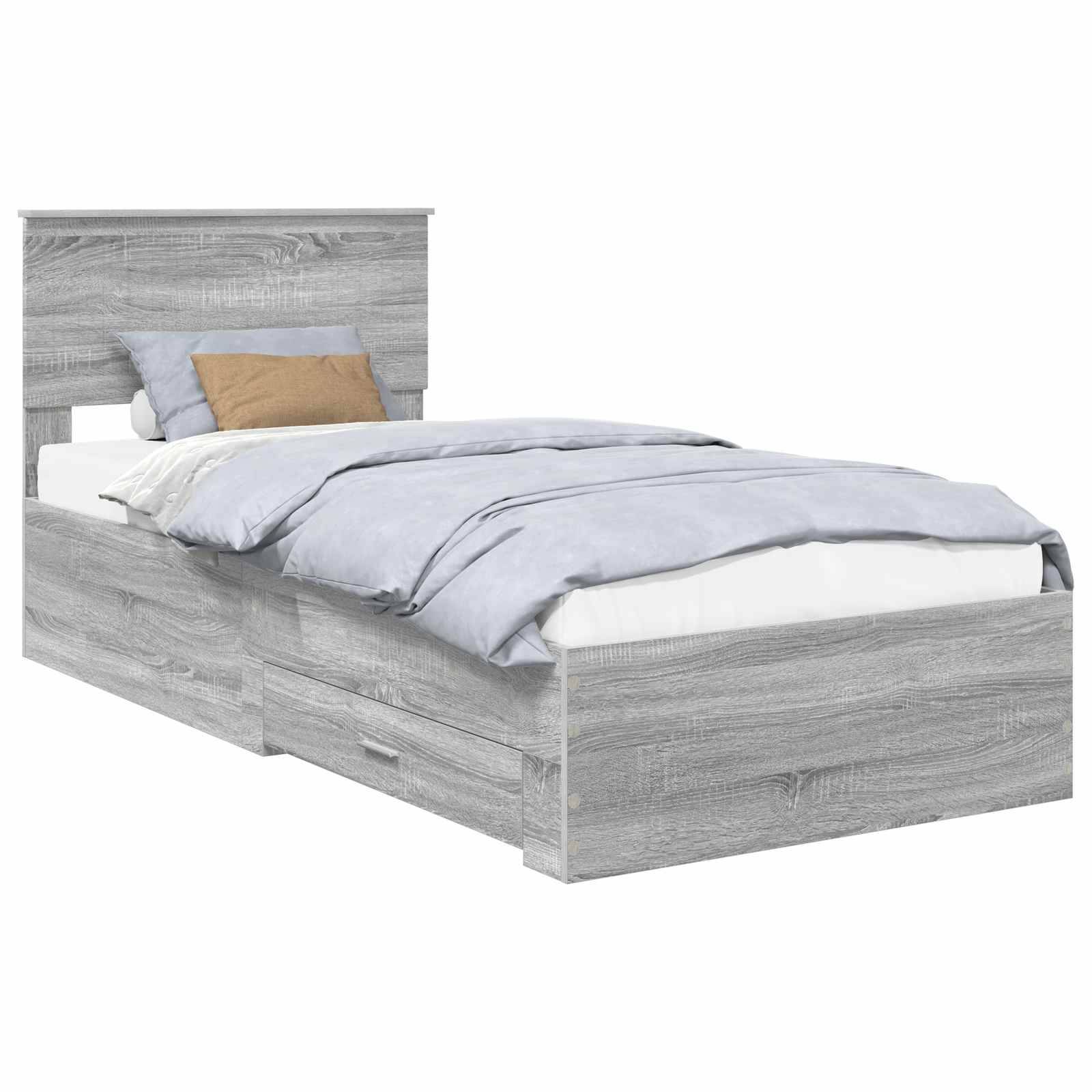 Ein grauer Holzbettrahmen mit Kopfteil, blaue Bettwäsche und zwei Bettschubladen. Ein beiger und ein weißes Kissen liegen auf dem Bett.